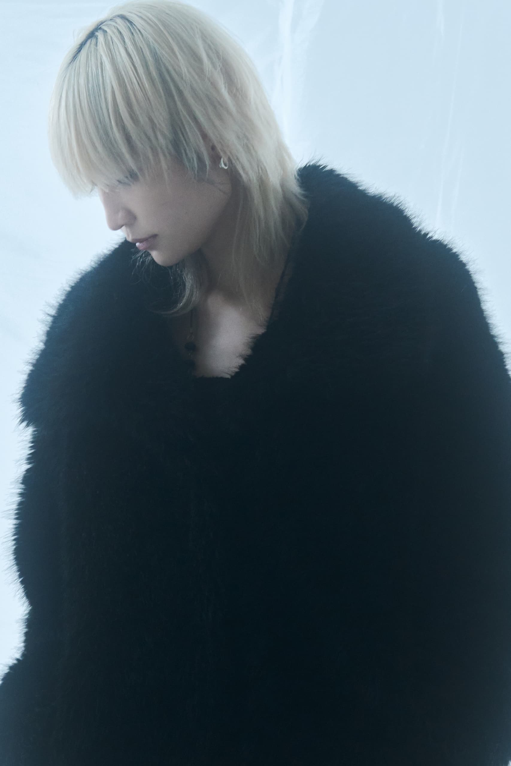 Individual in black fur coat with blonde hair against a soft white background.