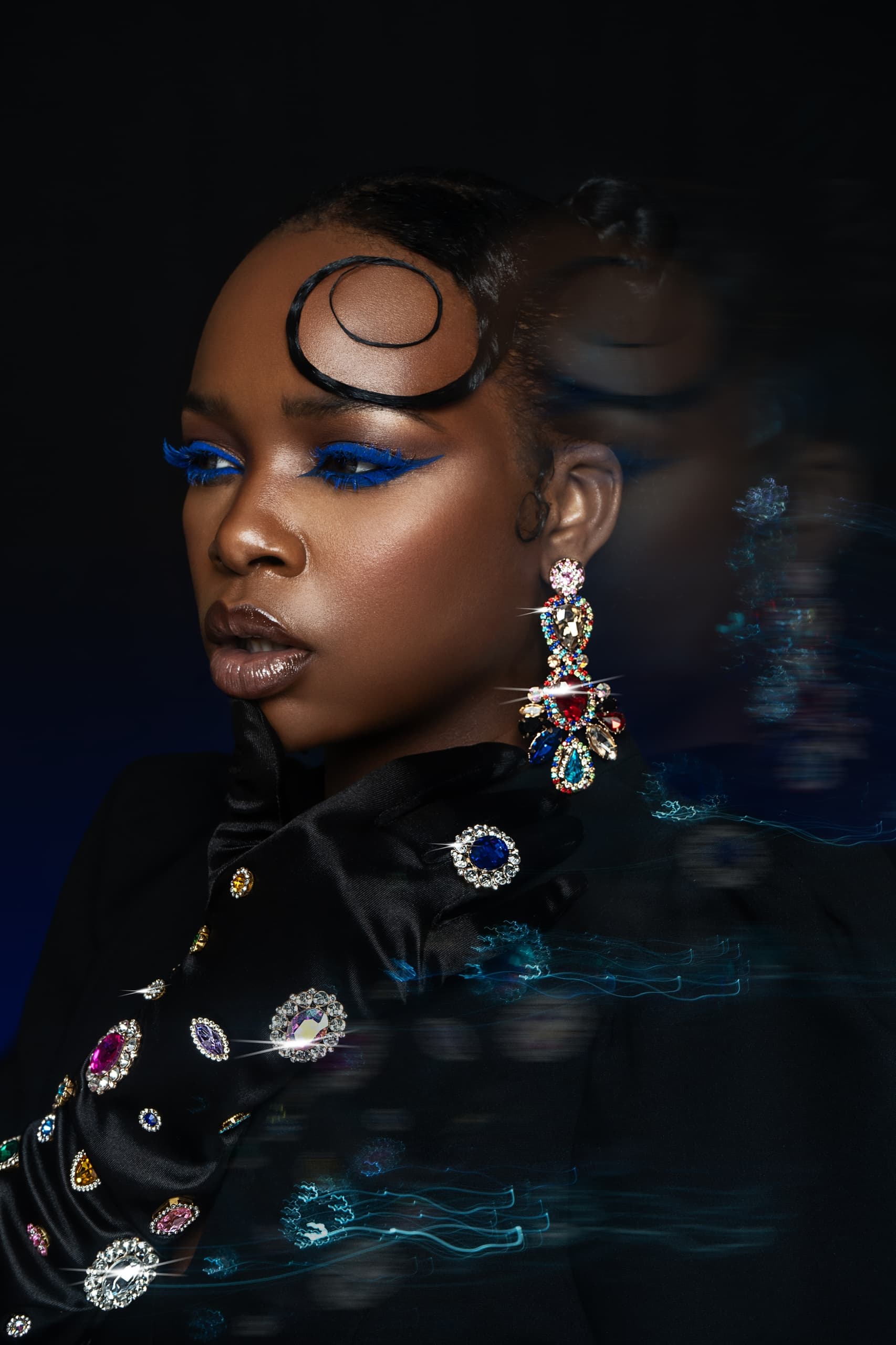 Glamorous woman with bold blue eyeshadow and sparkling jewelry in a striking pose.