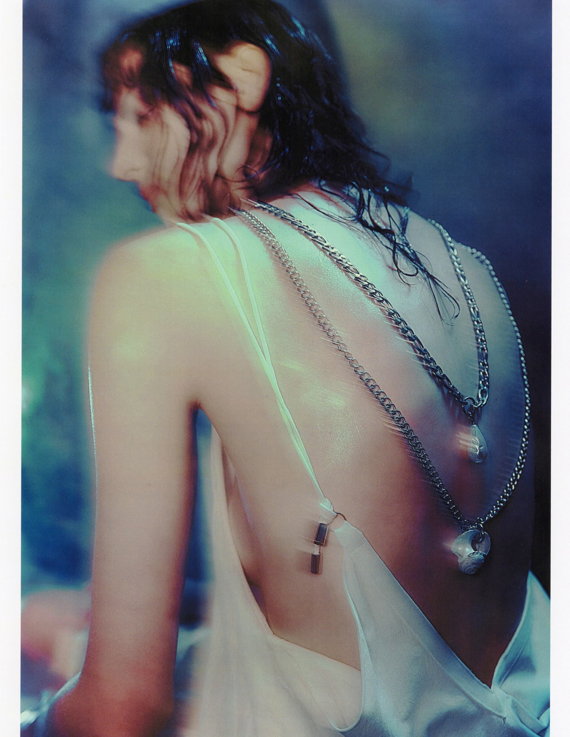 Fashionable woman in silky dress with layered necklaces, artistic lighting.