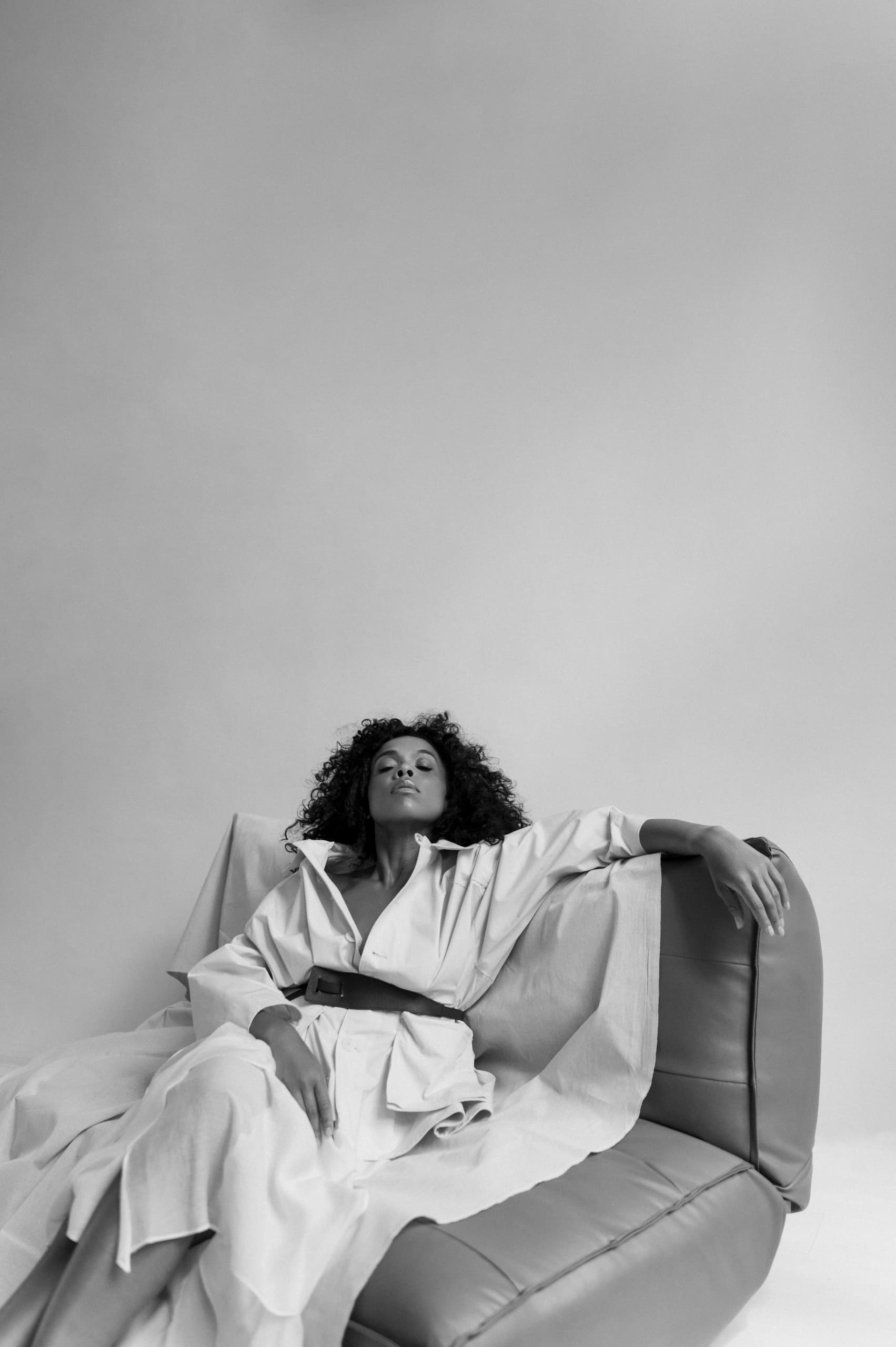 Person lounging stylishly on a leather couch in a minimalist setting.
