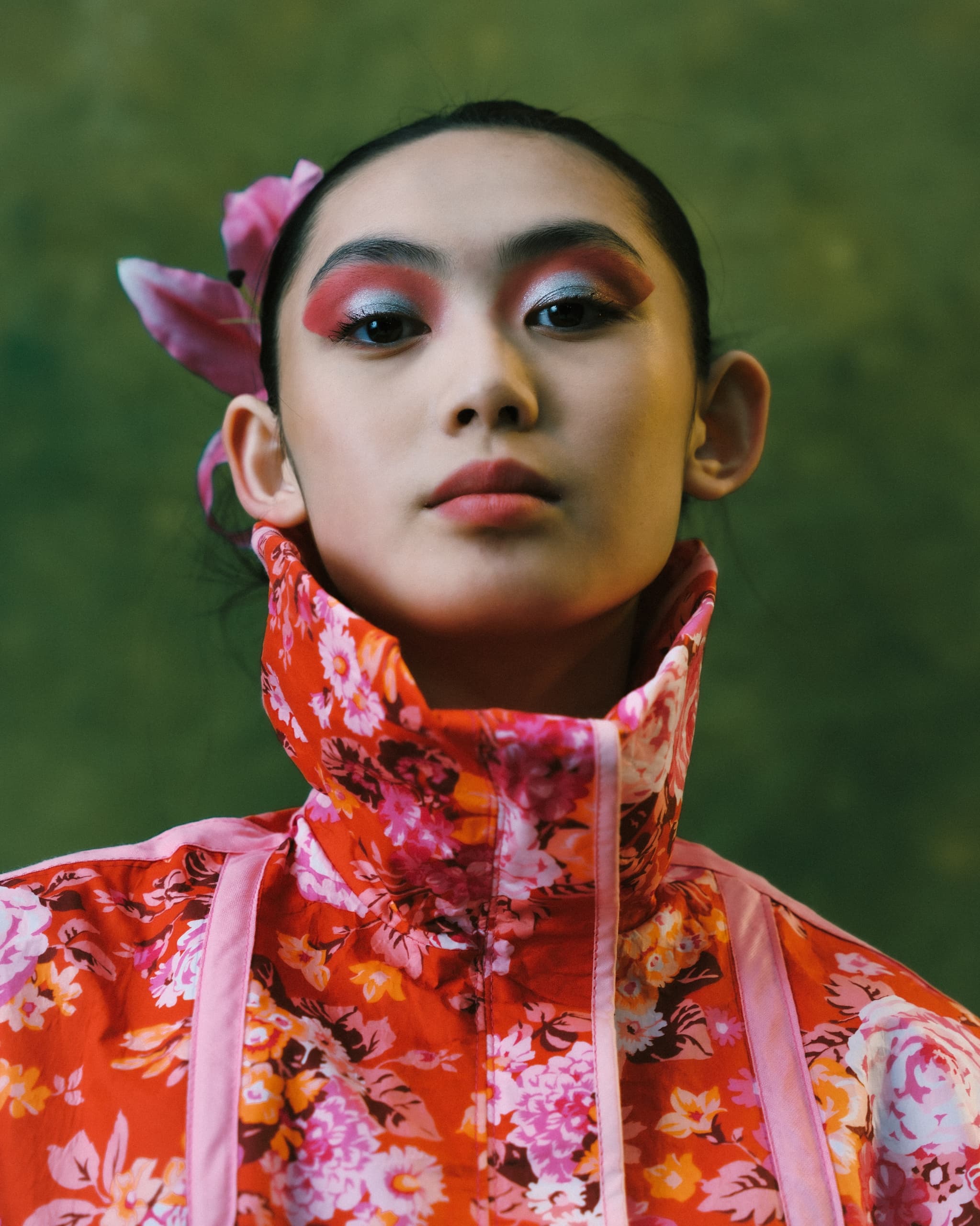 Fashion model in vibrant floral outfit with bold makeup on green background.
