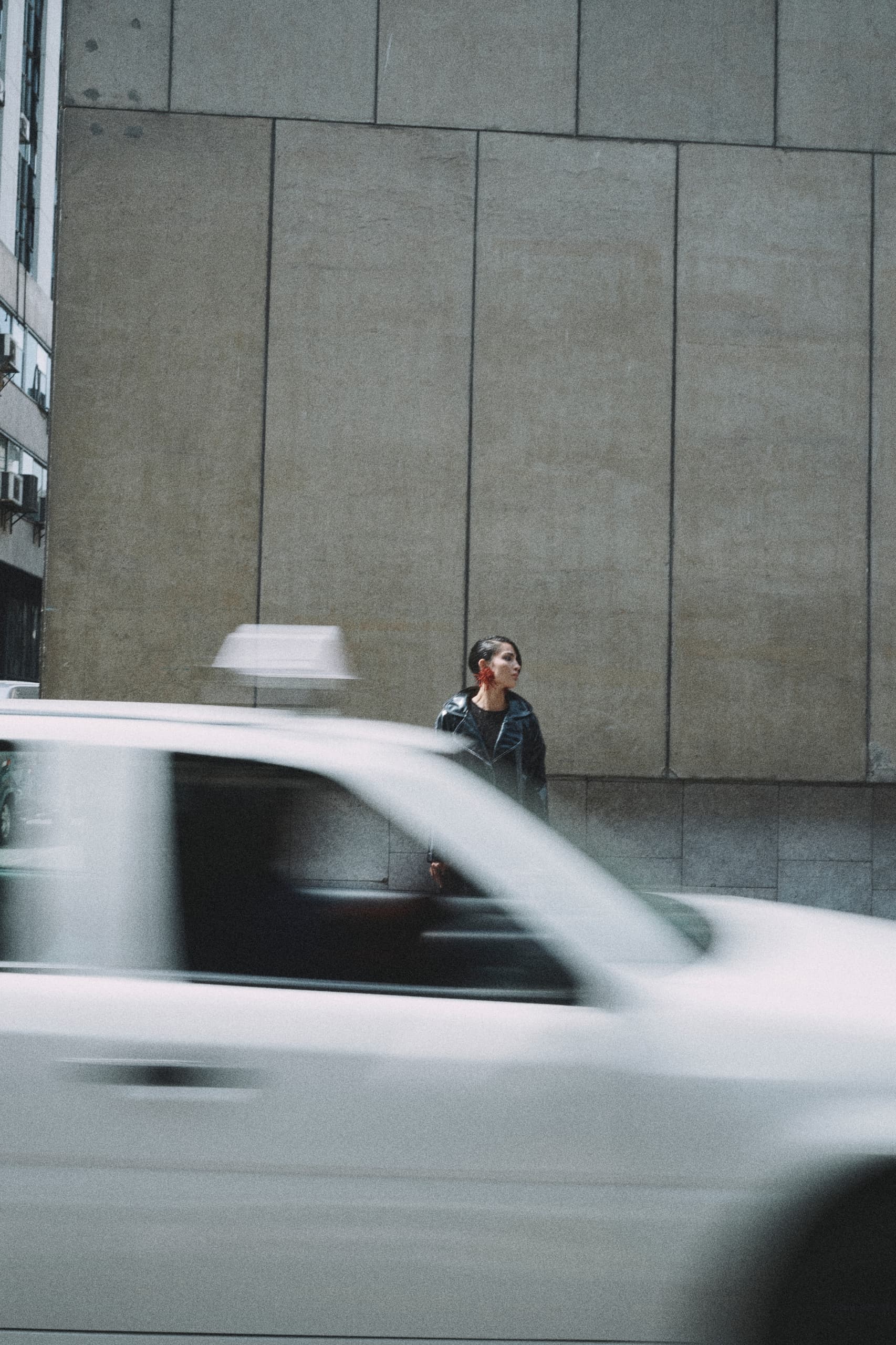 Woman stands by moving taxi on urban street with large wall background.
