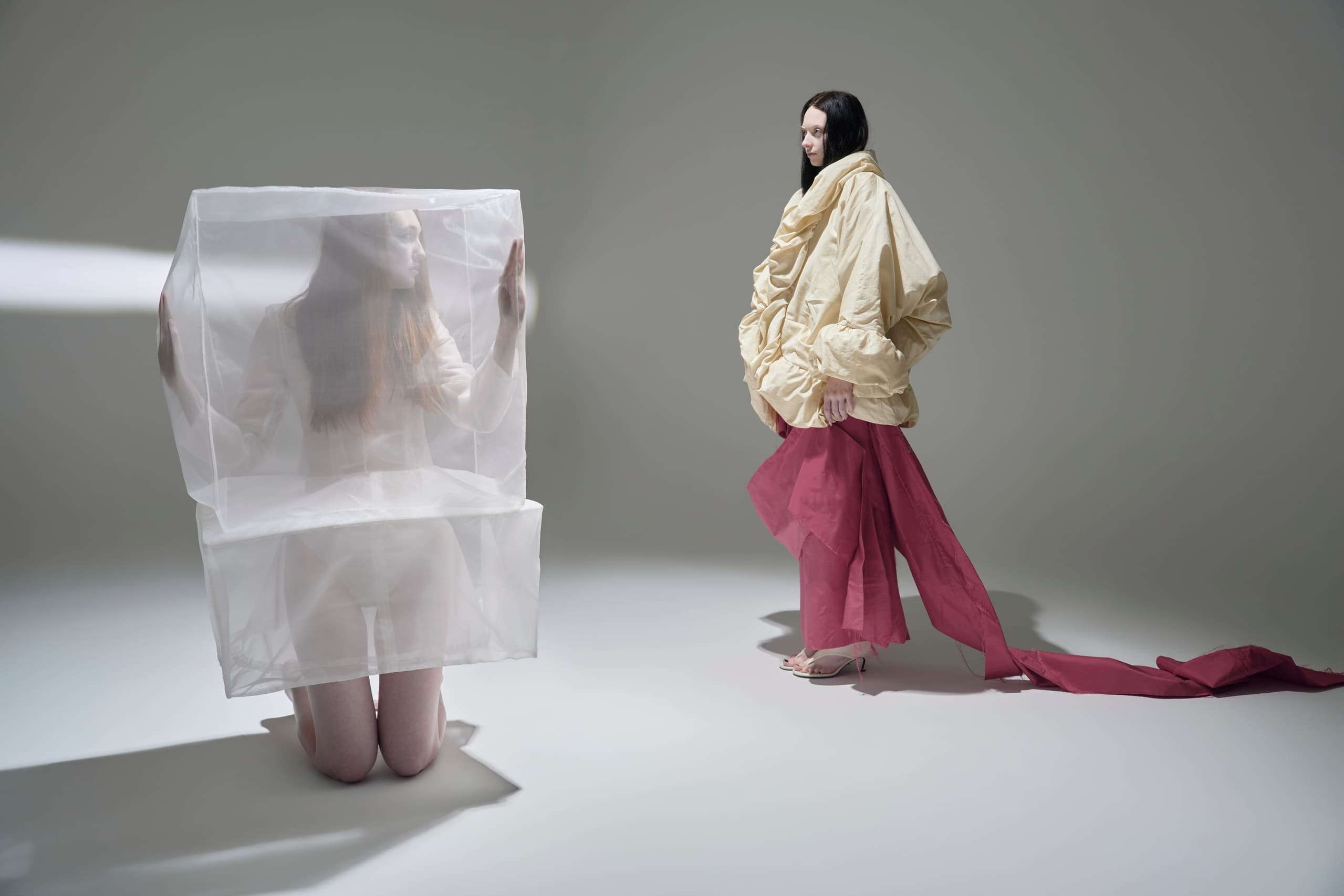Two models in artistic fashion, one in sheer, one in ruffled clothes, create a unique scene.