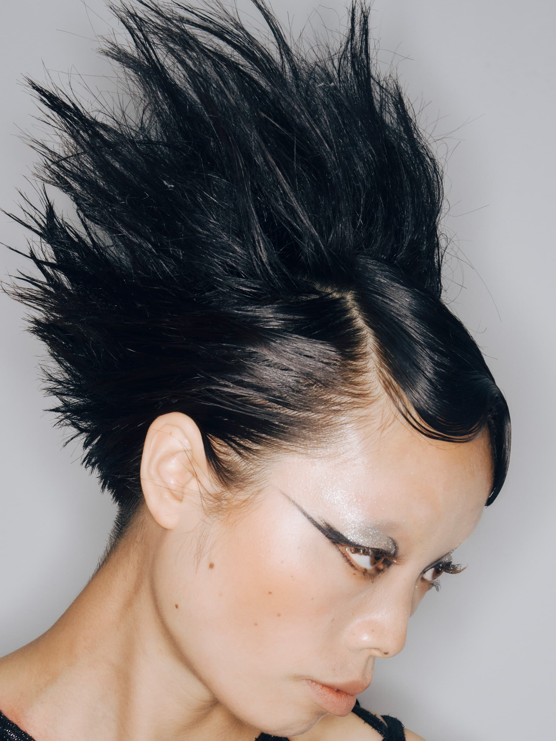 Edgy spiked hairstyle with dramatic eyeliner and sleek makeup.