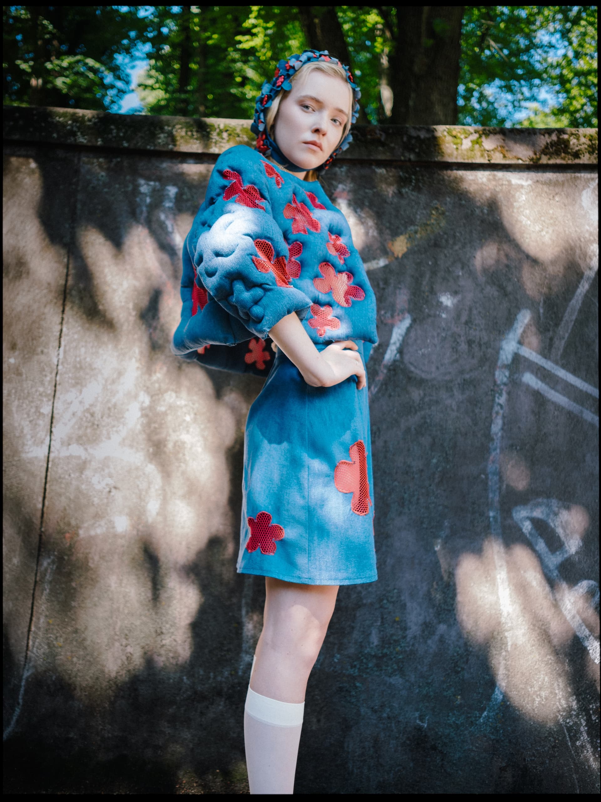 Fashionable woman in blue floral outfit posing against a shaded wall background.