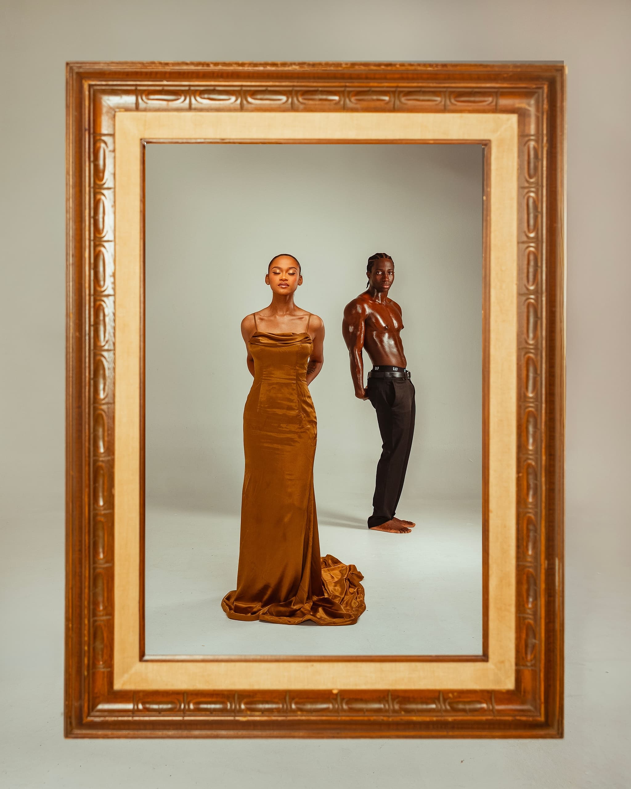 Stylish duo in gold gown and black pants framed elegantly in ornate picture frame.