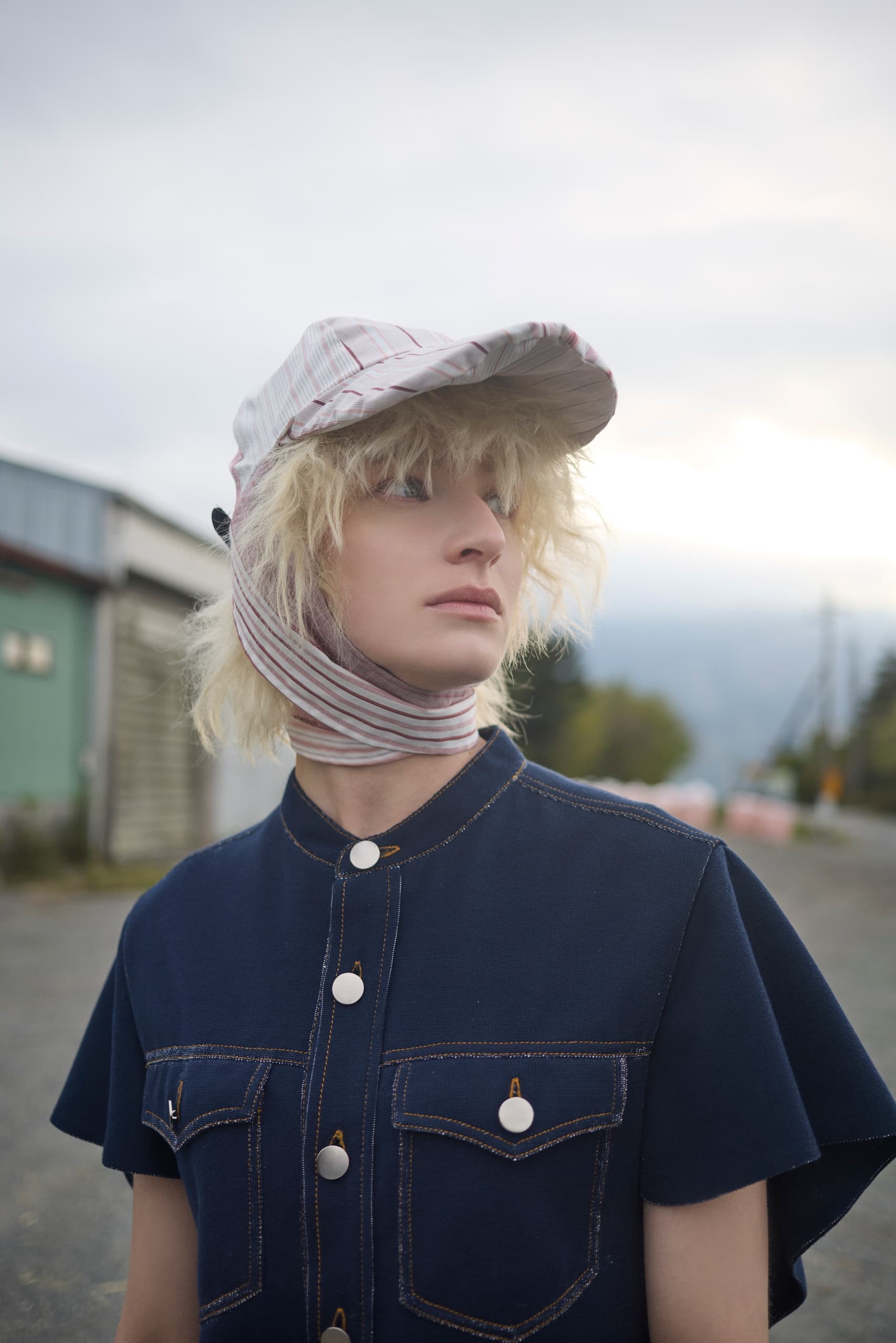 Person in blue outfit and striped cap outdoors, fashion photography.