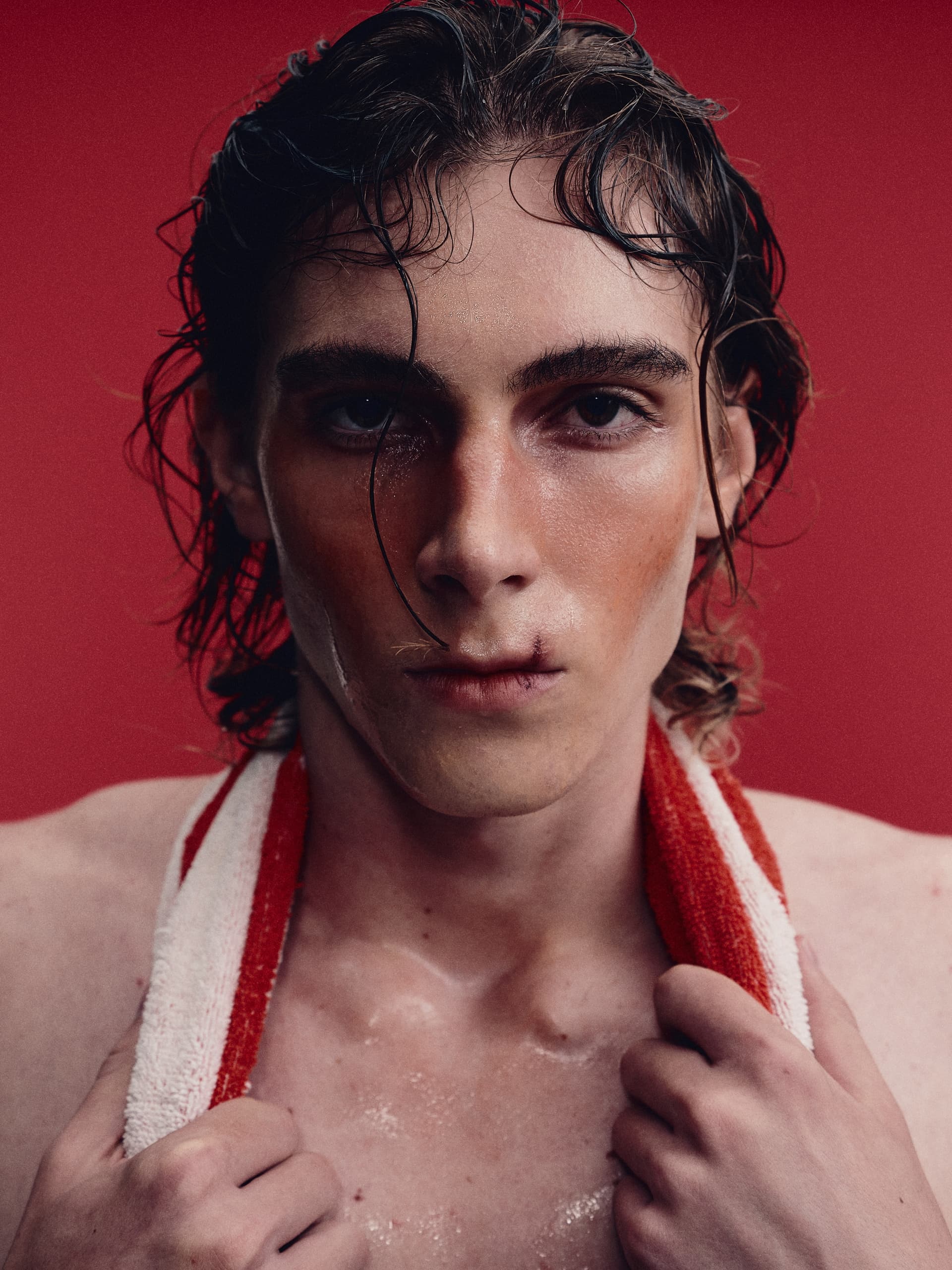 Man with wet hair and towel against red background, intense expression.