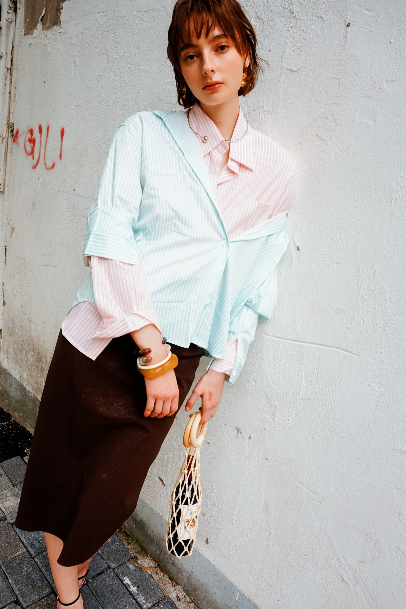 Fashionable woman in striped shirt and brown skirt holding a wine bag by graffiti wall.