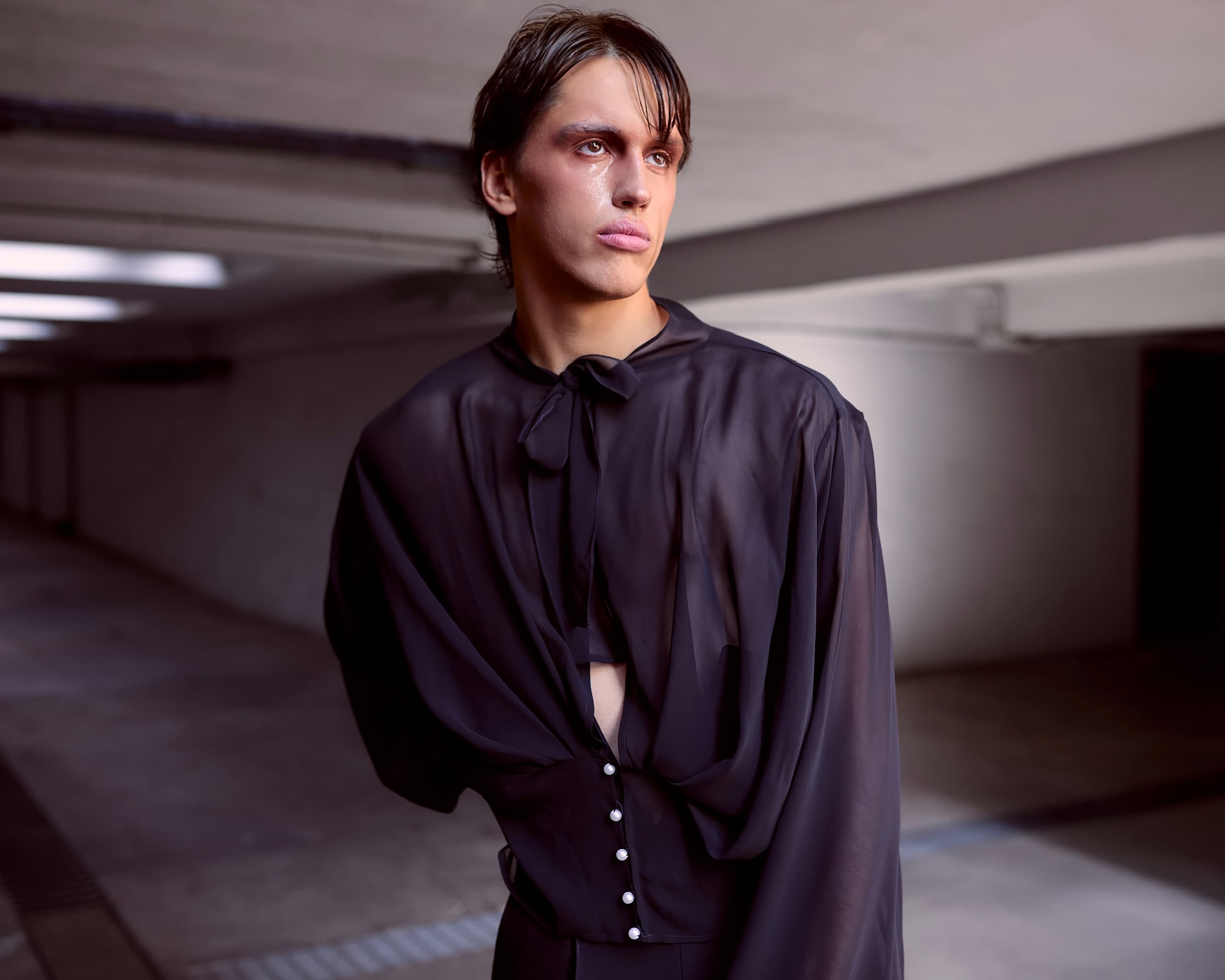 Person in a sheer black blouse posing in an urban setting.