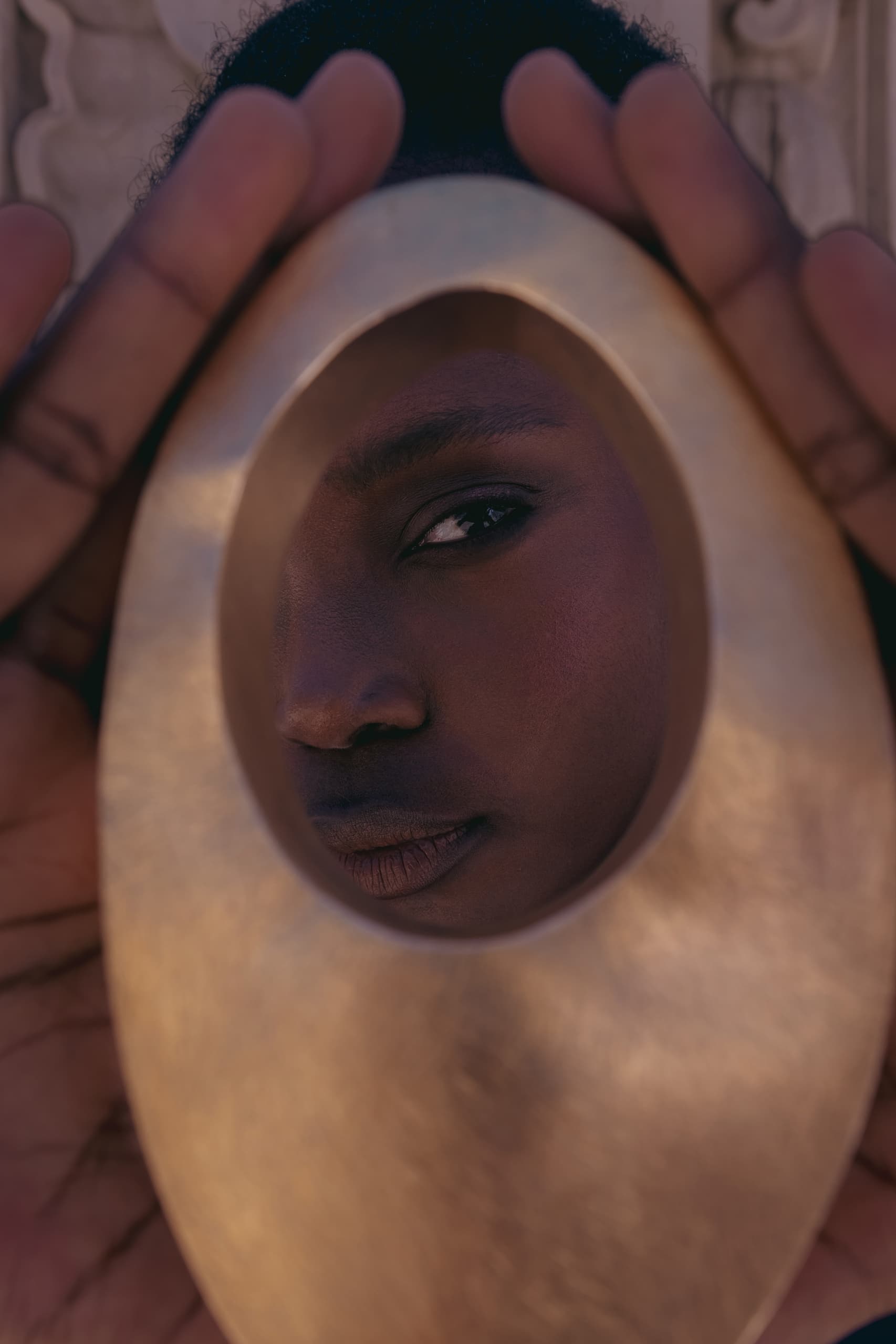 A person's eye seen through an oval cutout in a golden object, creating a unique frame.