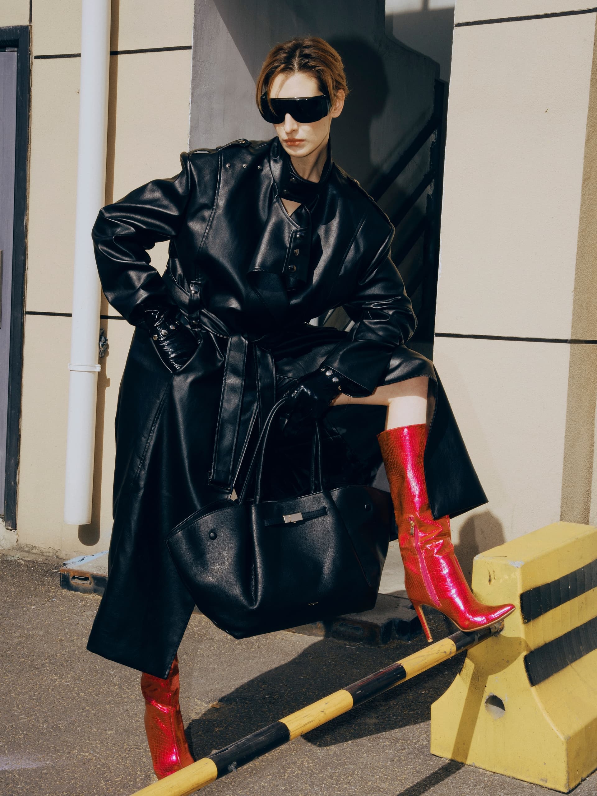 Stylish woman in black leather and red boots striking a pose next to a barrier.