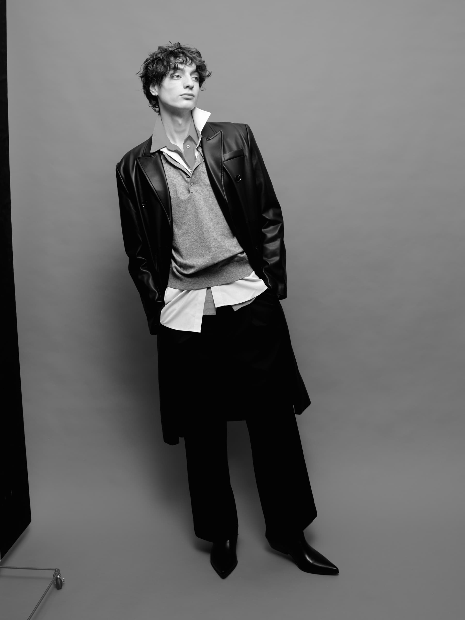 Fashionable man in layered clothing, leather jacket, gray background, black-and-white.