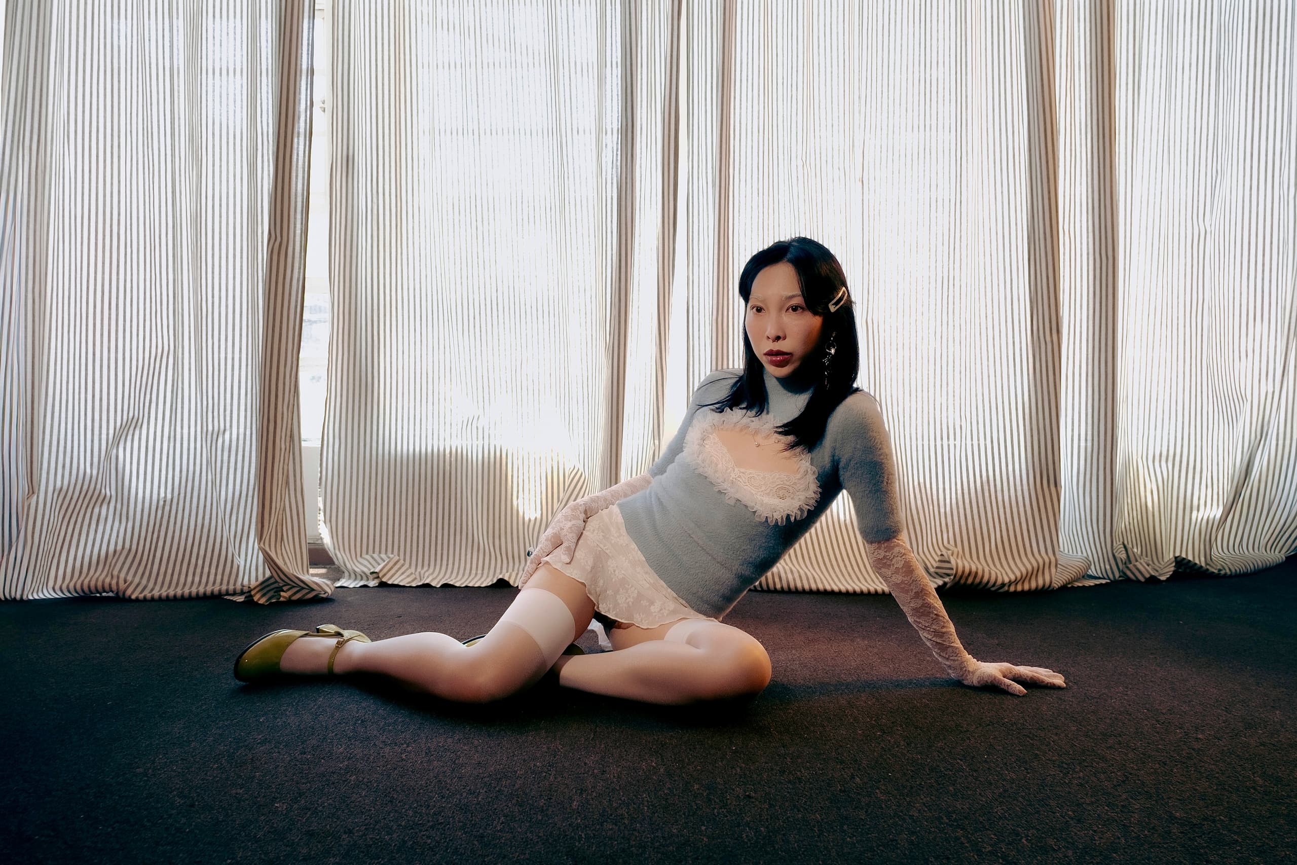 Person sitting on carpeted floor in front of striped curtains, wearing stylish outfit.
