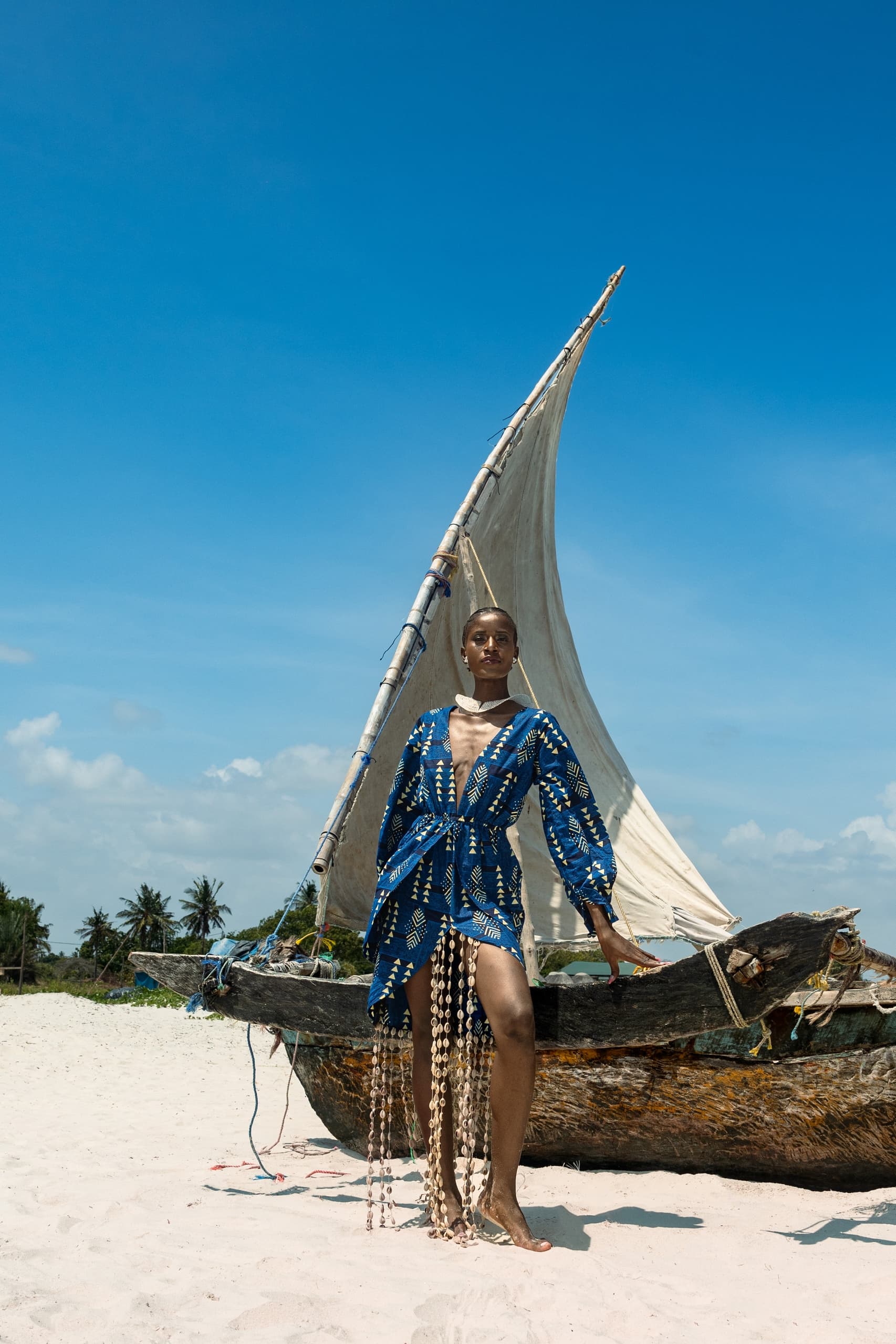 Fashionable woman in blue dress by a traditional boat on a sunny beach.