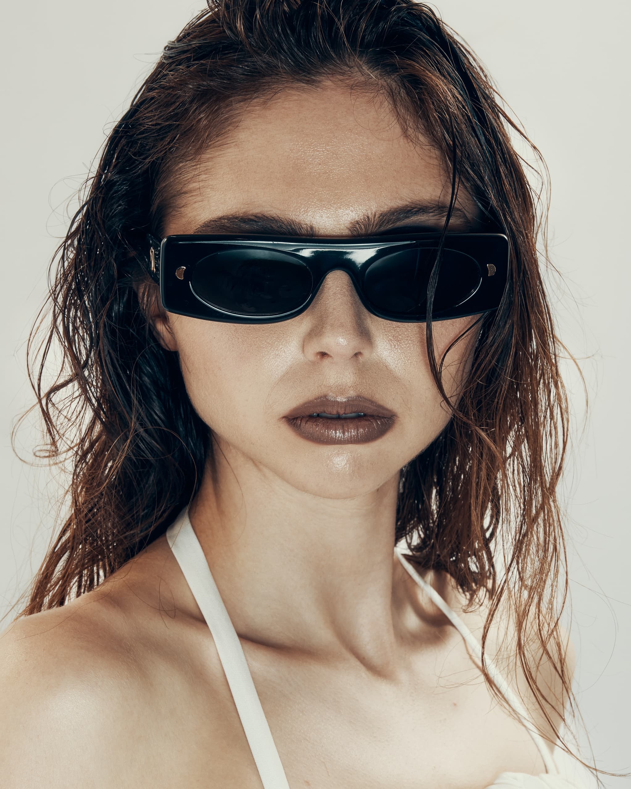 Person with wet hair wearing black sunglasses and white top, confident expression.