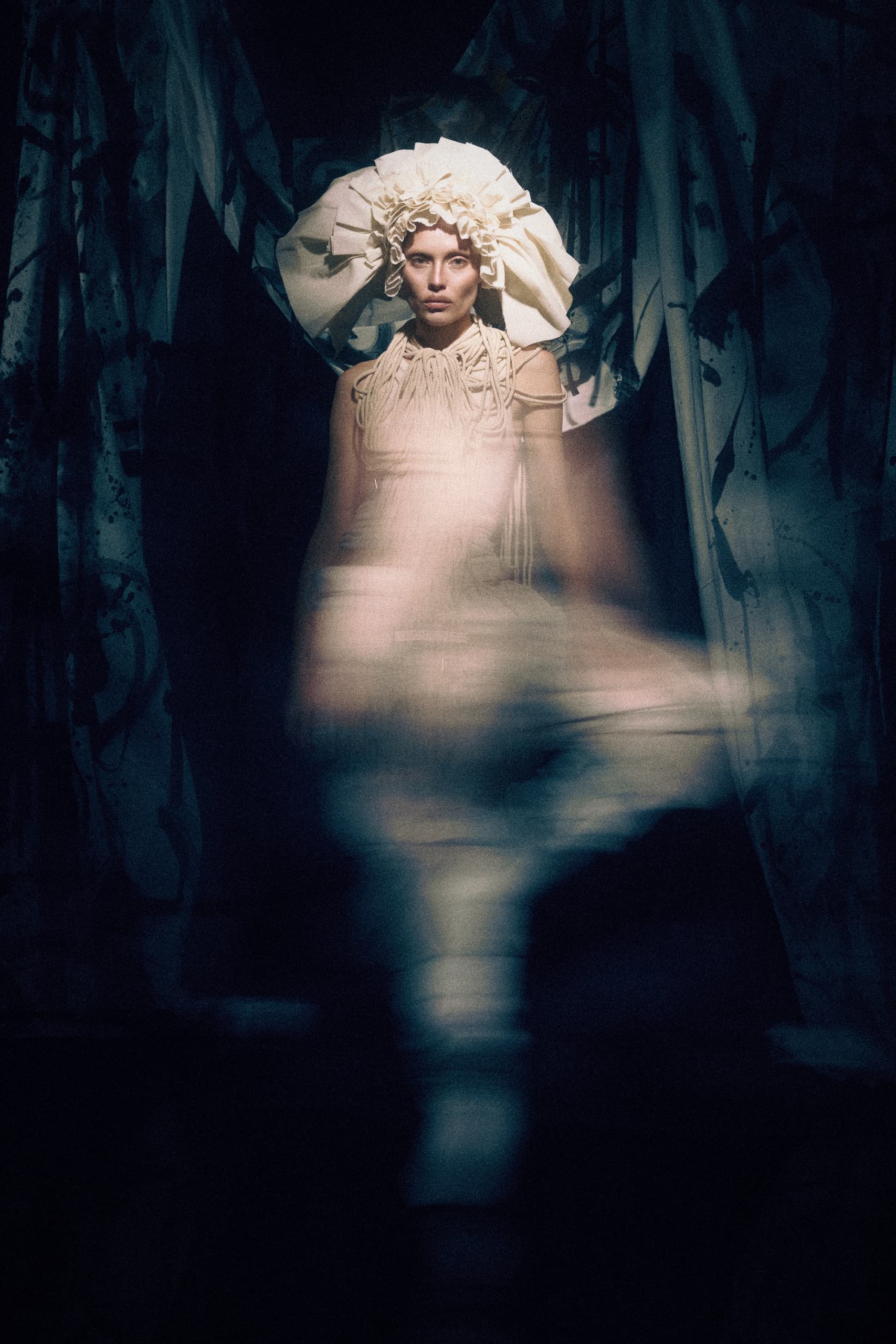 Avant-garde fashion: woman in artistic hat, ethereal blur effect, dark ambiance.