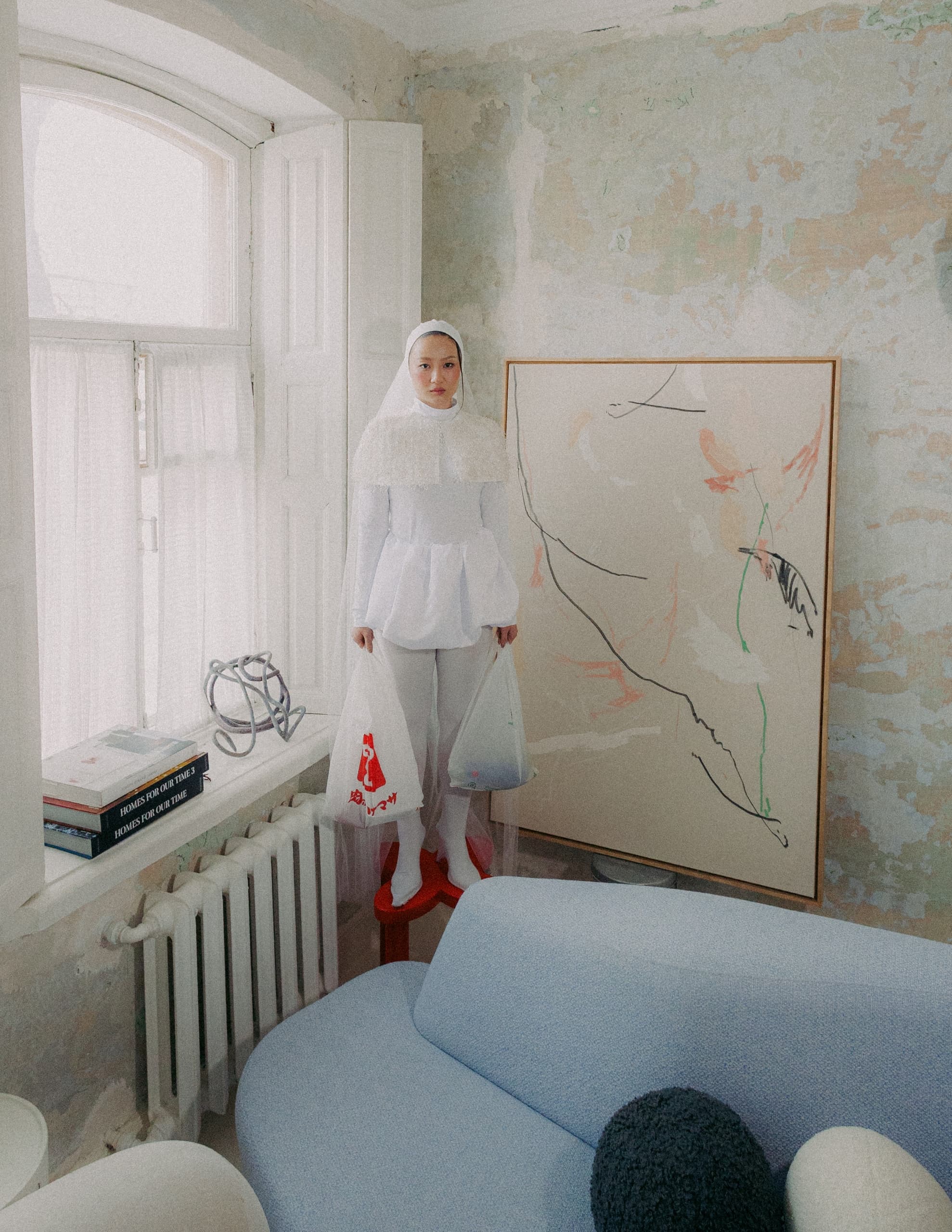 Person in artistic room, holding bags, standing near a large abstract painting.