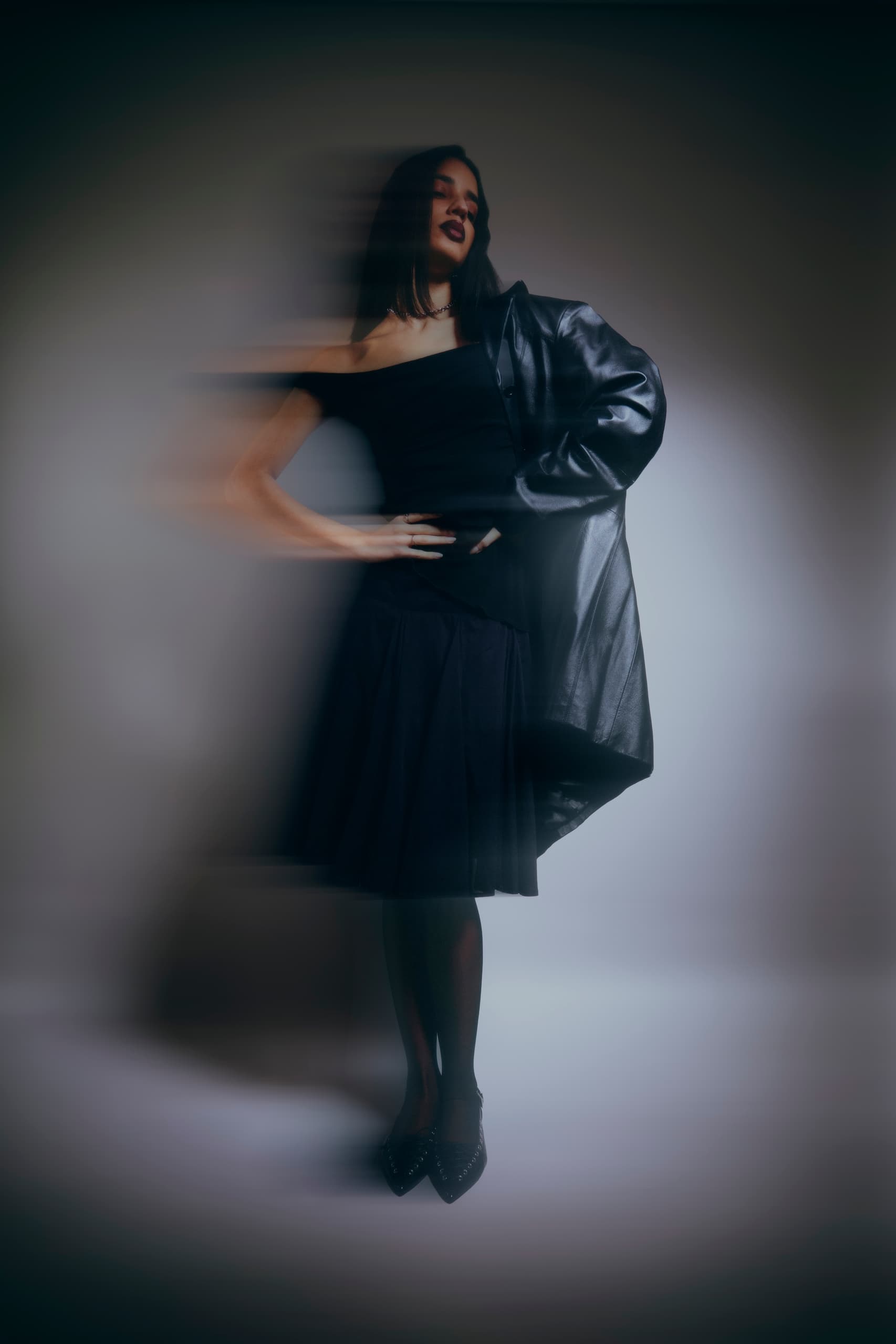 Stylish woman poses in black dress and leather jacket with motion blur effect.
