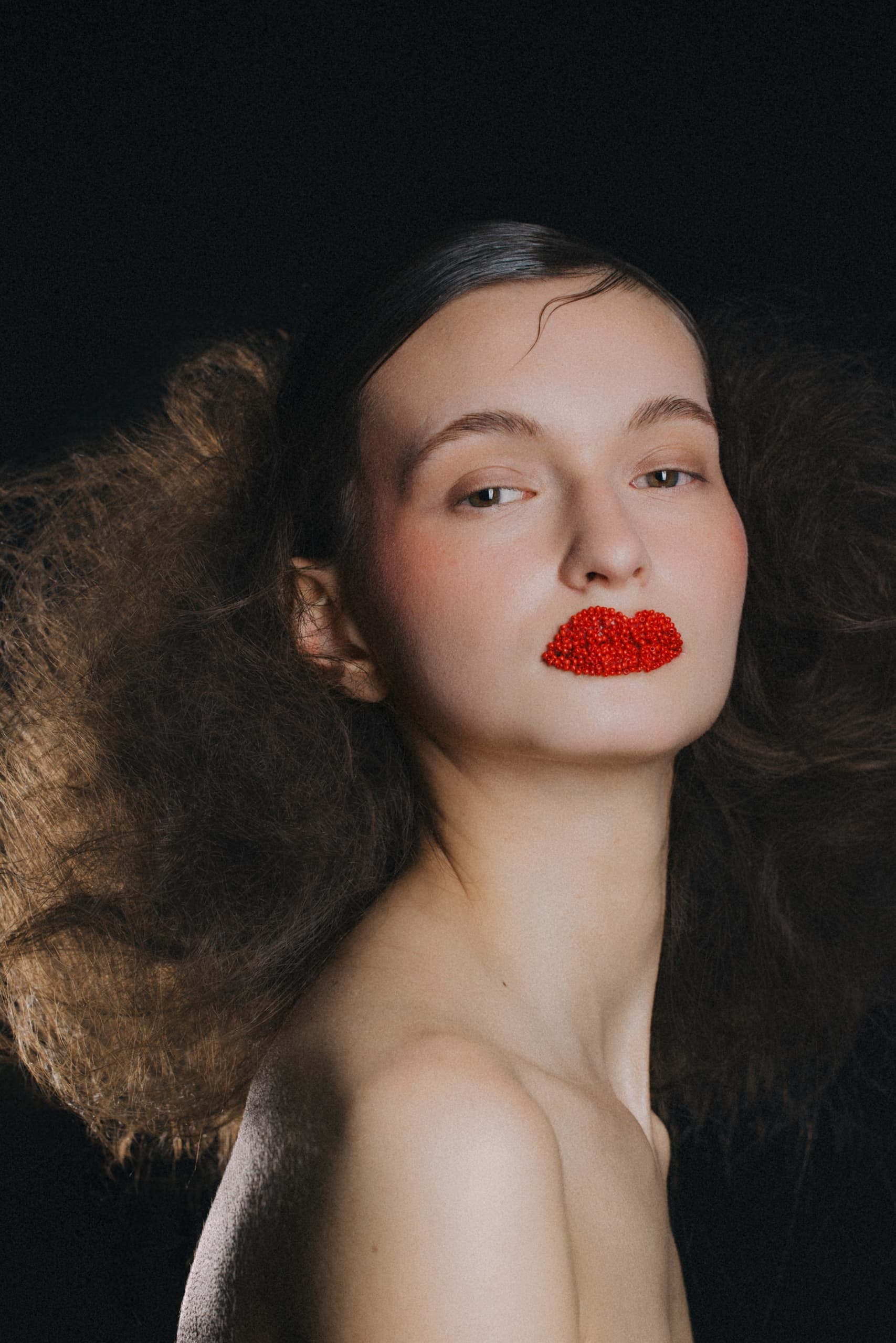 Model with bold red lips and voluminous hair on a dark background.