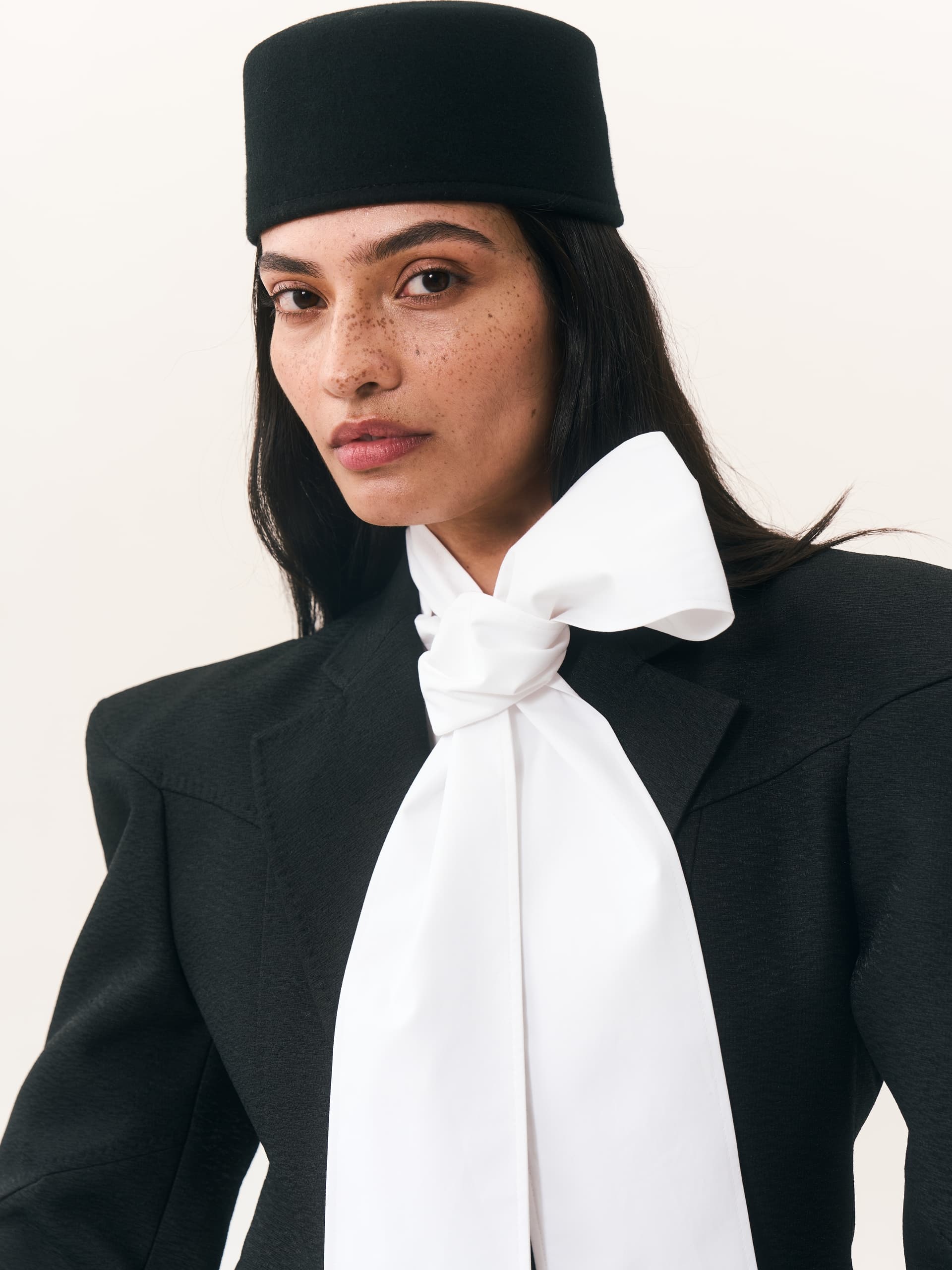 Stylish woman in a black hat and suit with a white bow tie.