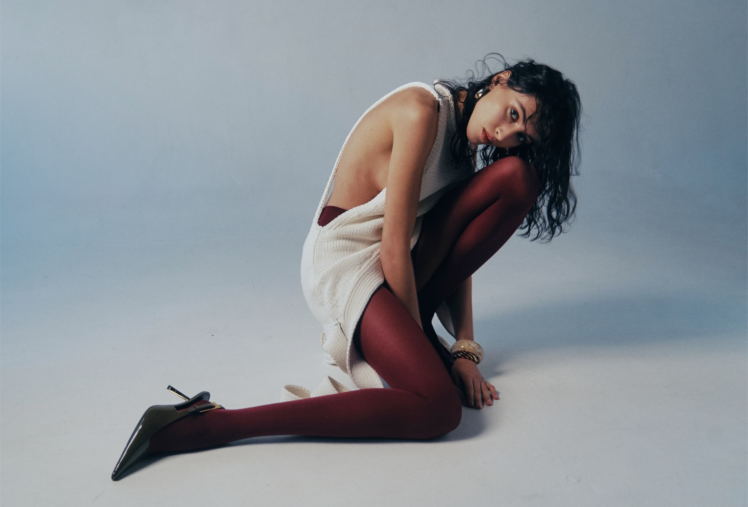 Fashion model in red tights and white dress posing on a light background.