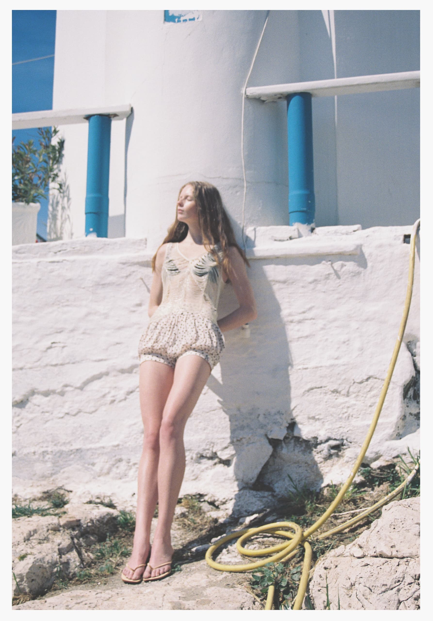 Woman in summer outfit leaning against a whitewashed wall