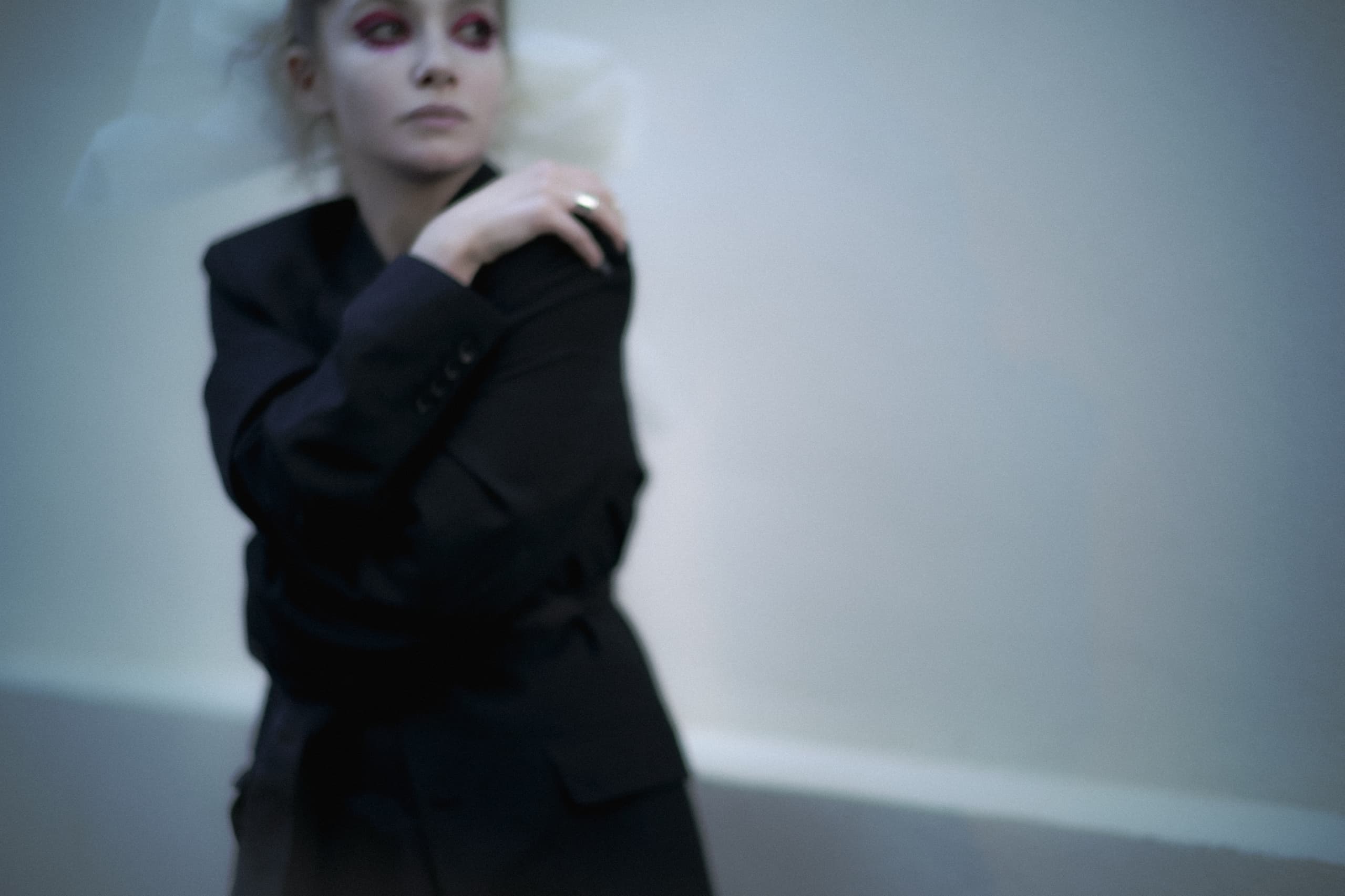 Blurry portrait of a woman in a dark suit with dramatic makeup.