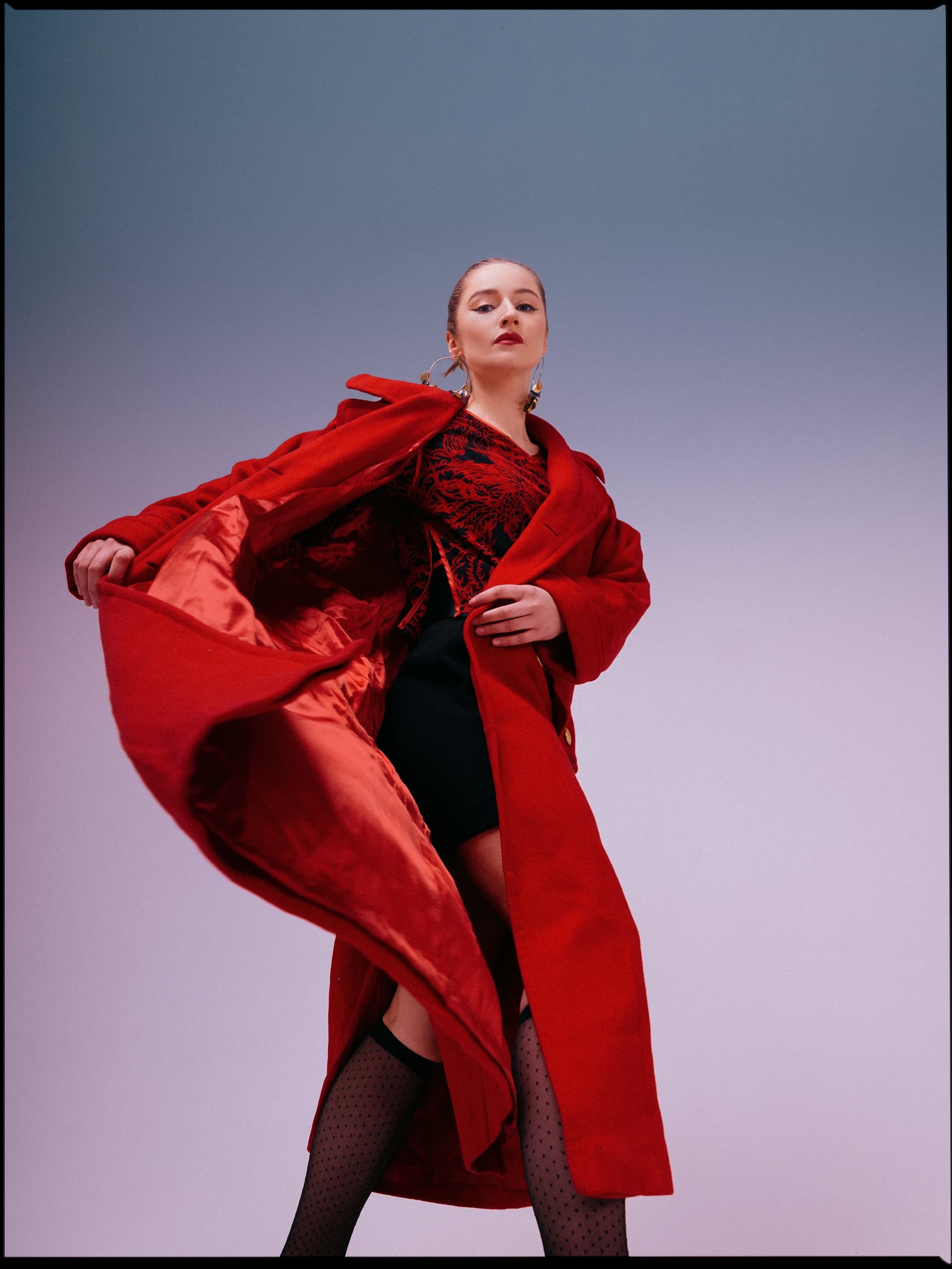 Fashionable woman in a red coat striking a confident pose against a gradient background.