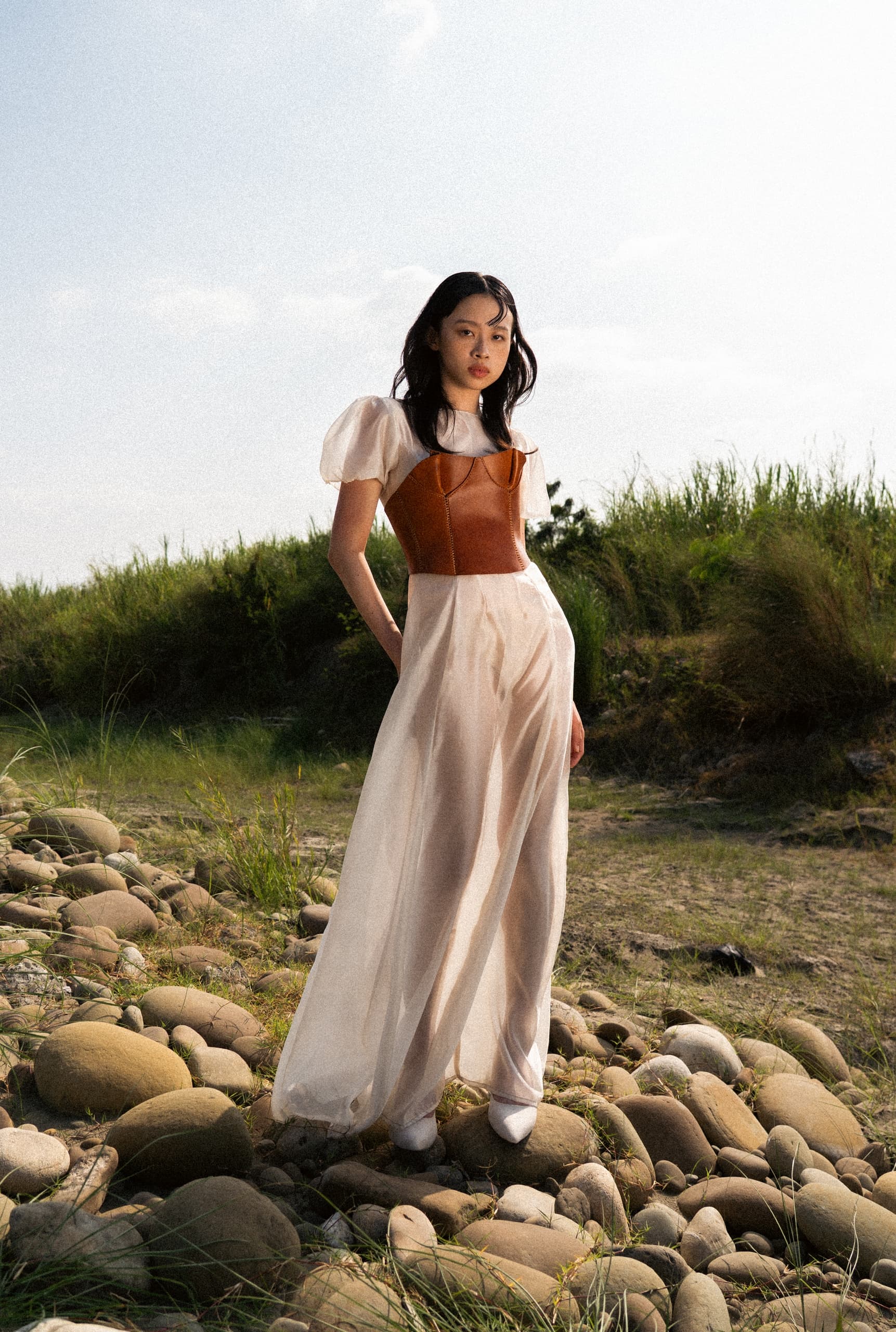 Woman in elegant fashion poses in scenic outdoor landscape.