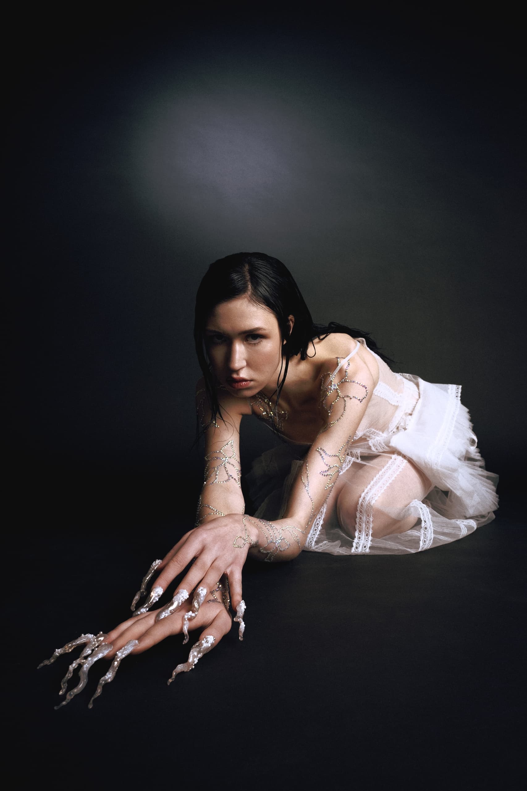 Person in artistic pose wearing textured white dress, intricate nail design.