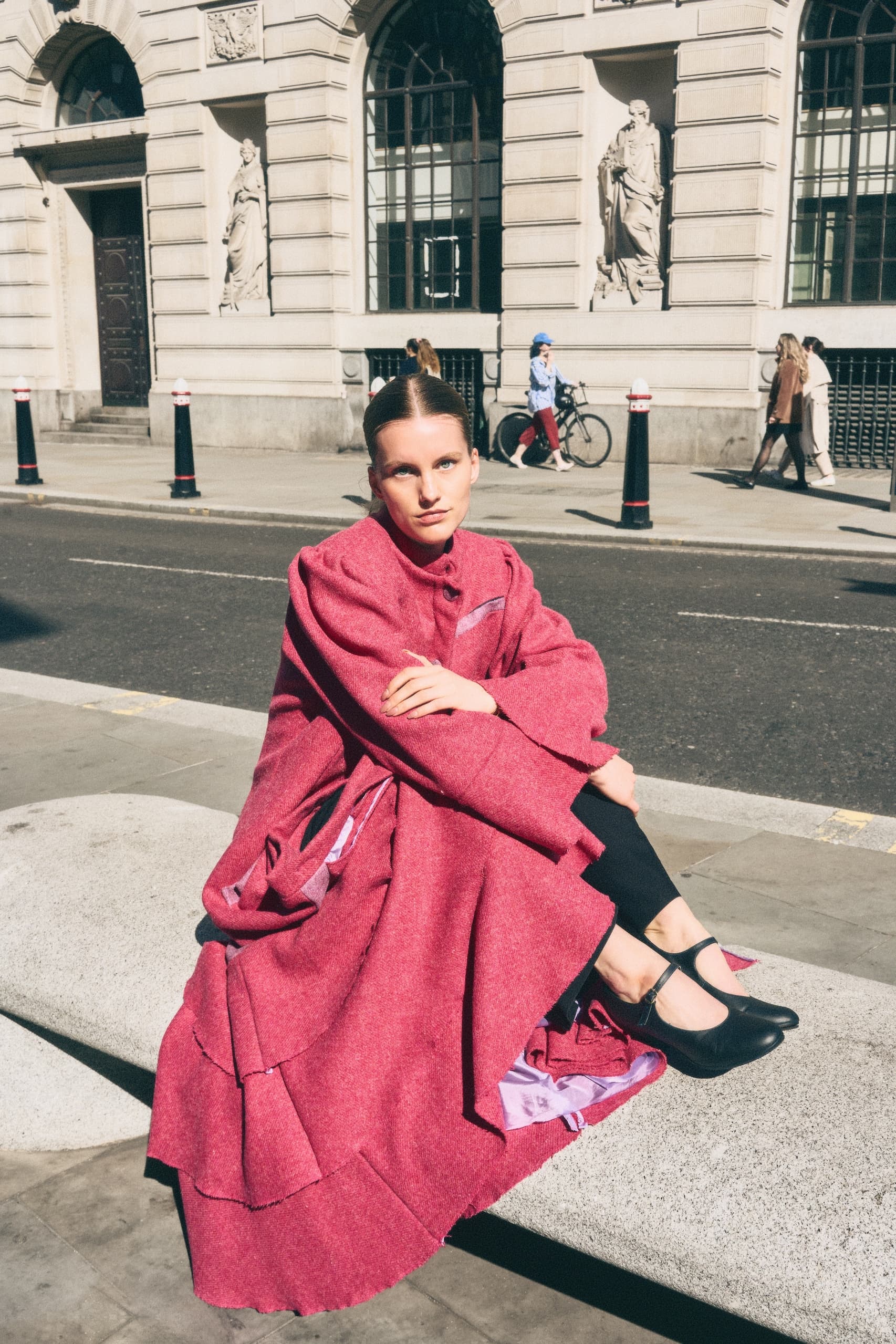 Woman in vibrant red dress sitting on urban street bench in a cityscape setting.