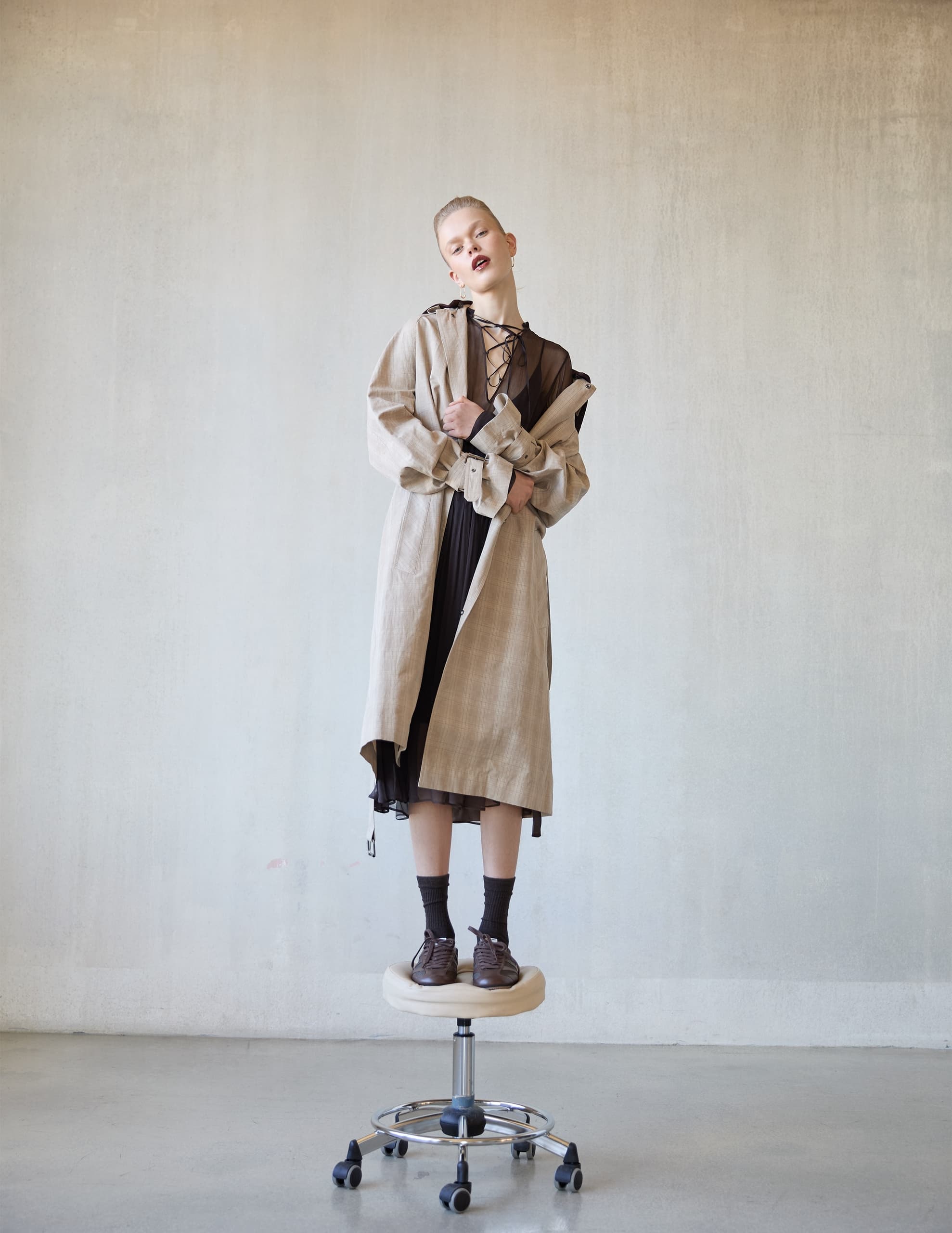 Fashionable person in trench coat standing on a stool, minimalist background.