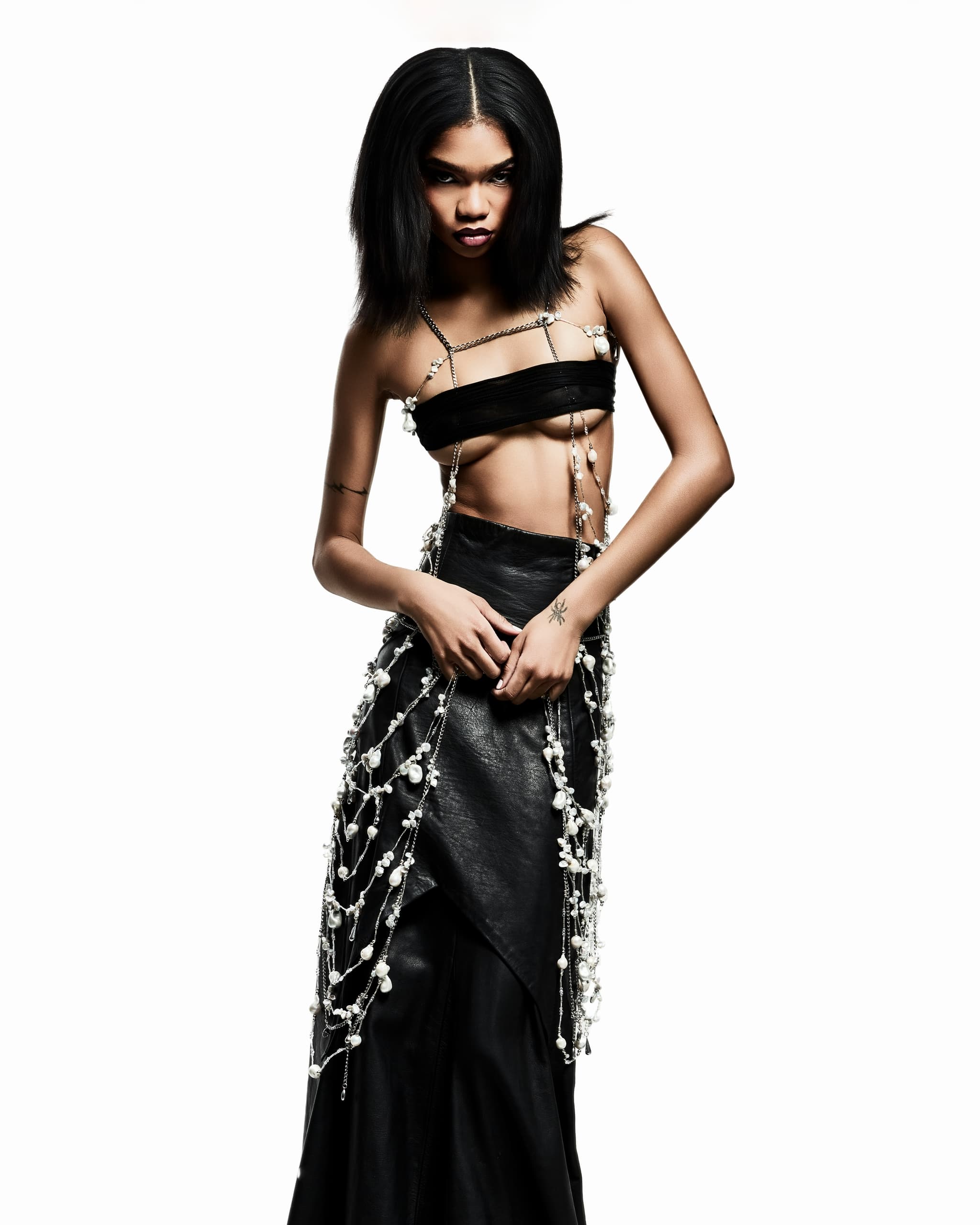 Fashion model in a chic black outfit with pearl accents, striking a bold pose.