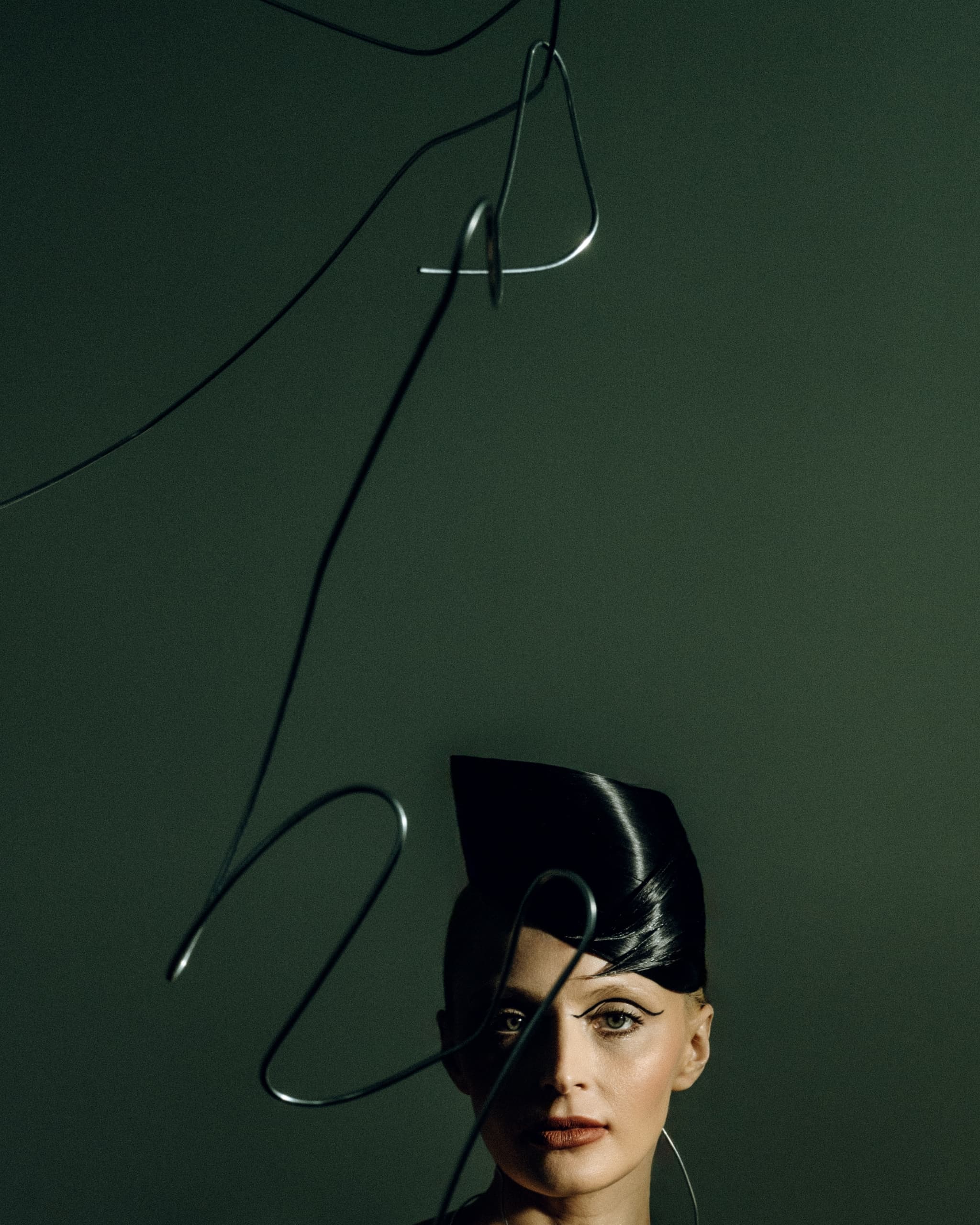 Avant-garde portrait with abstract wire and futuristic hairstyle on dark green background.