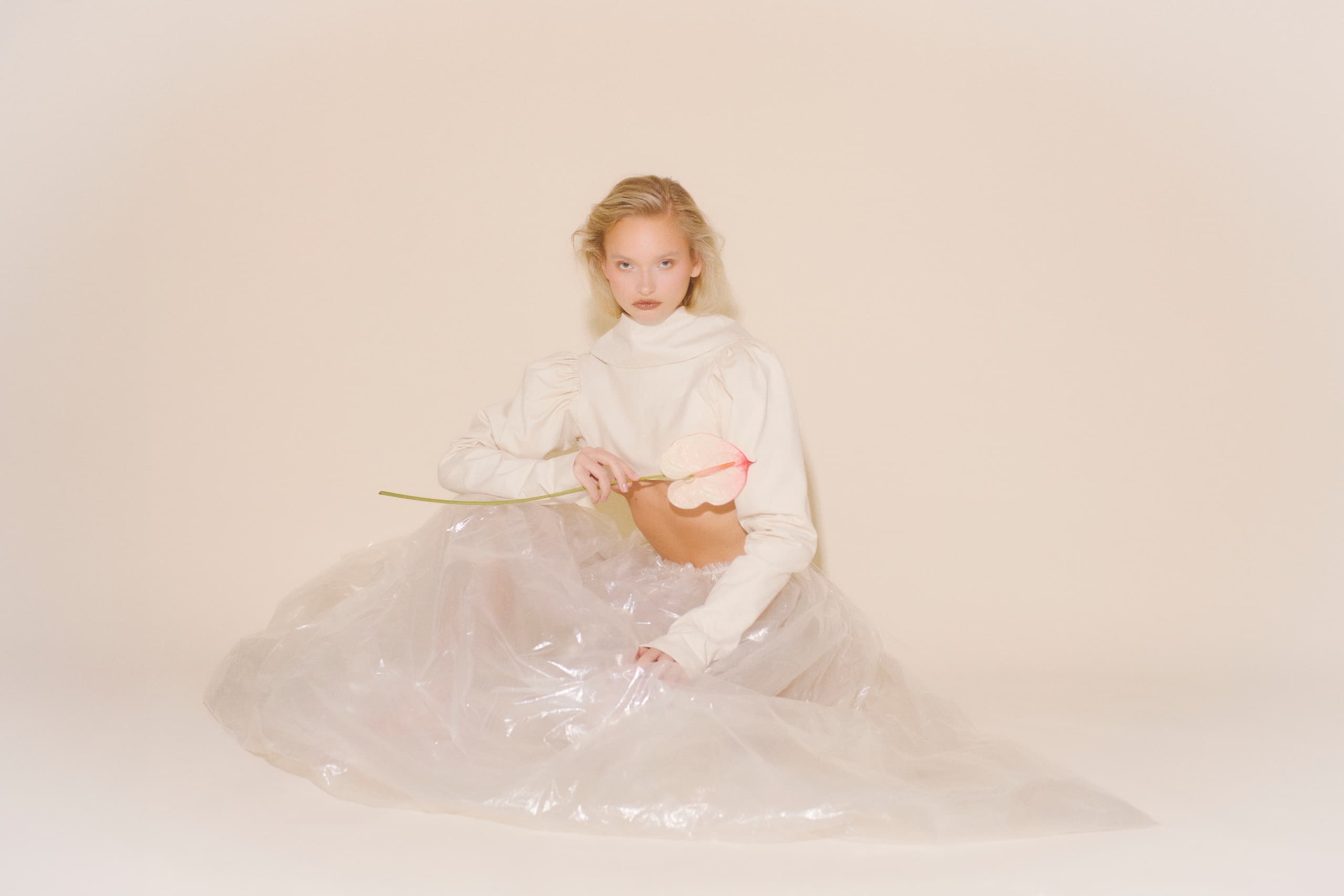 Elegant woman in sheer dress holding a pink flower in a minimalist setting.