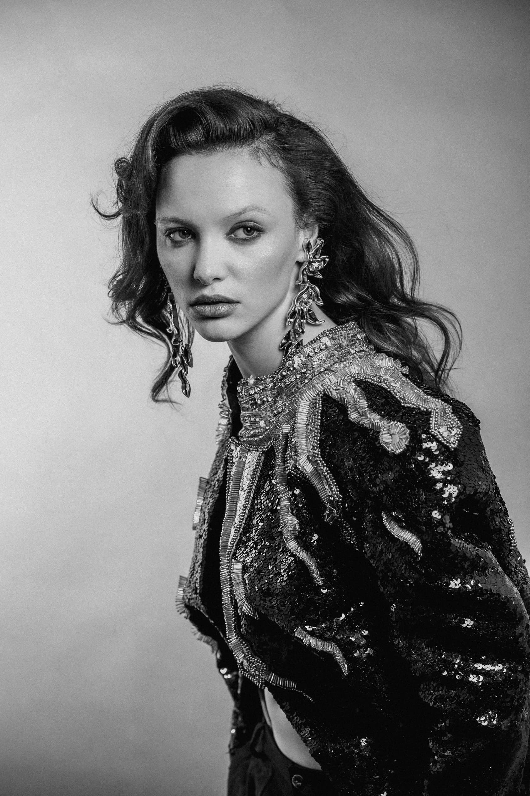 Elegant woman in sequined jacket, dramatic black and white portrait.