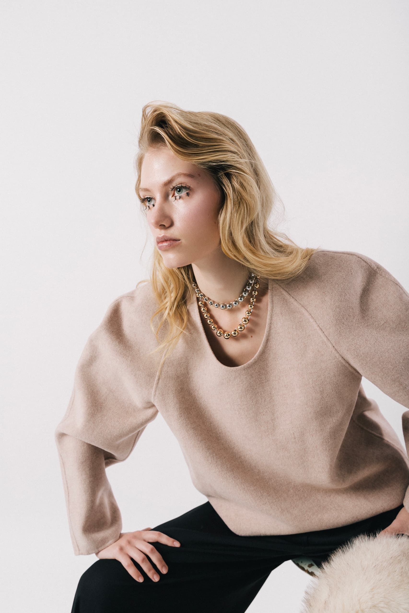 Fashionable woman in beige sweater with layered necklaces.