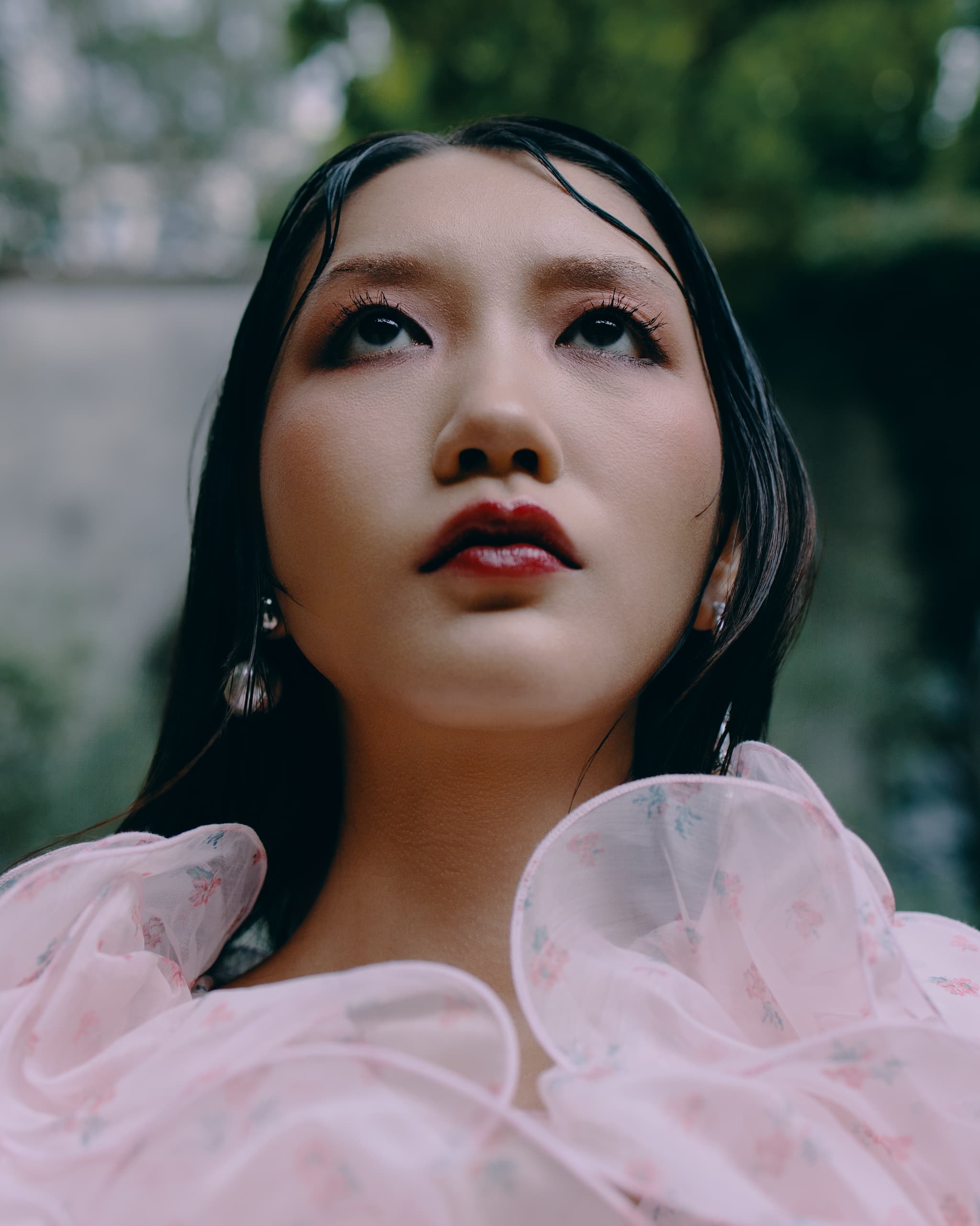 Woman gazing upwards, wearing floral pink dress, outdoors.