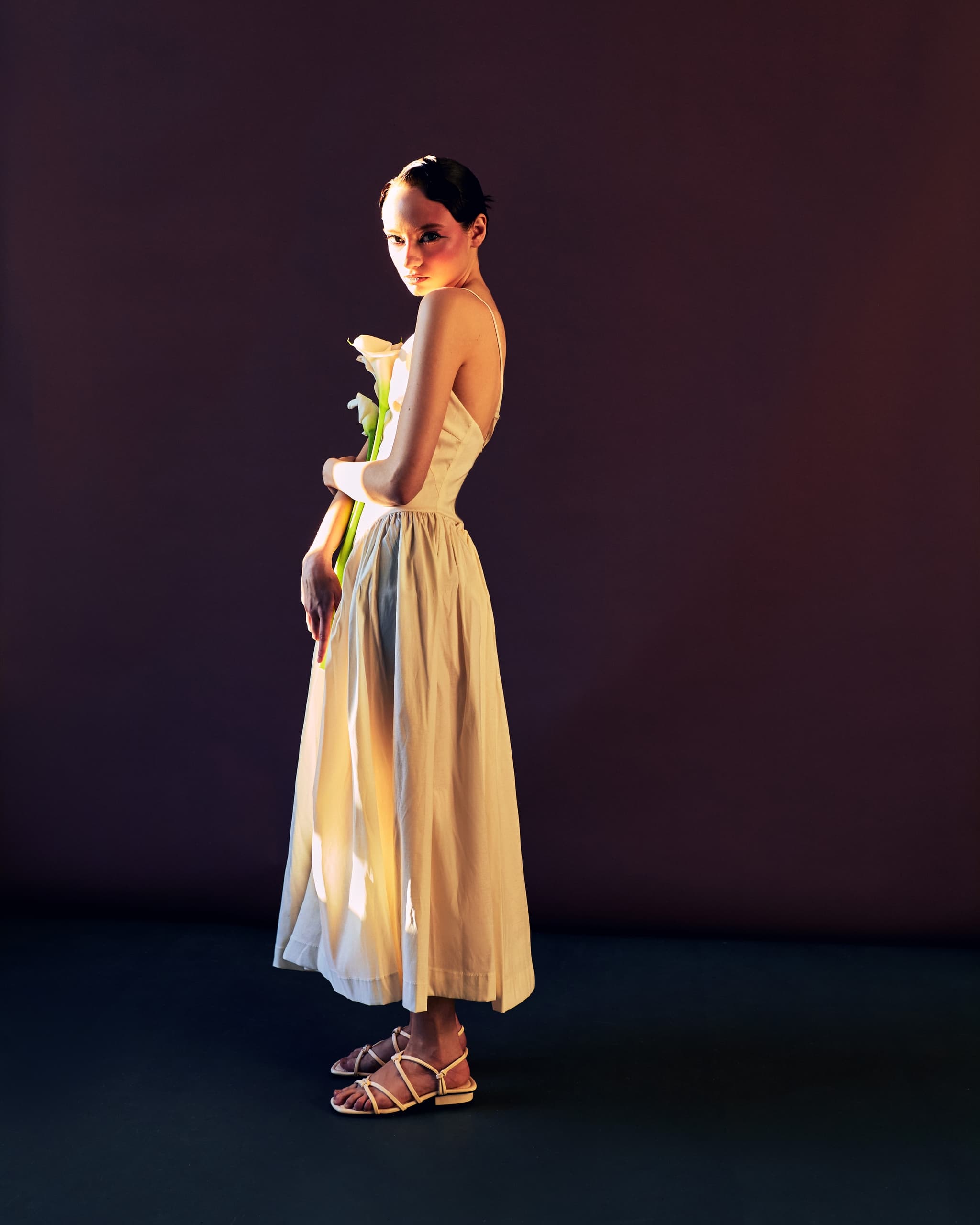 Woman in cream dress holding a calla lily in dramatic lighting.