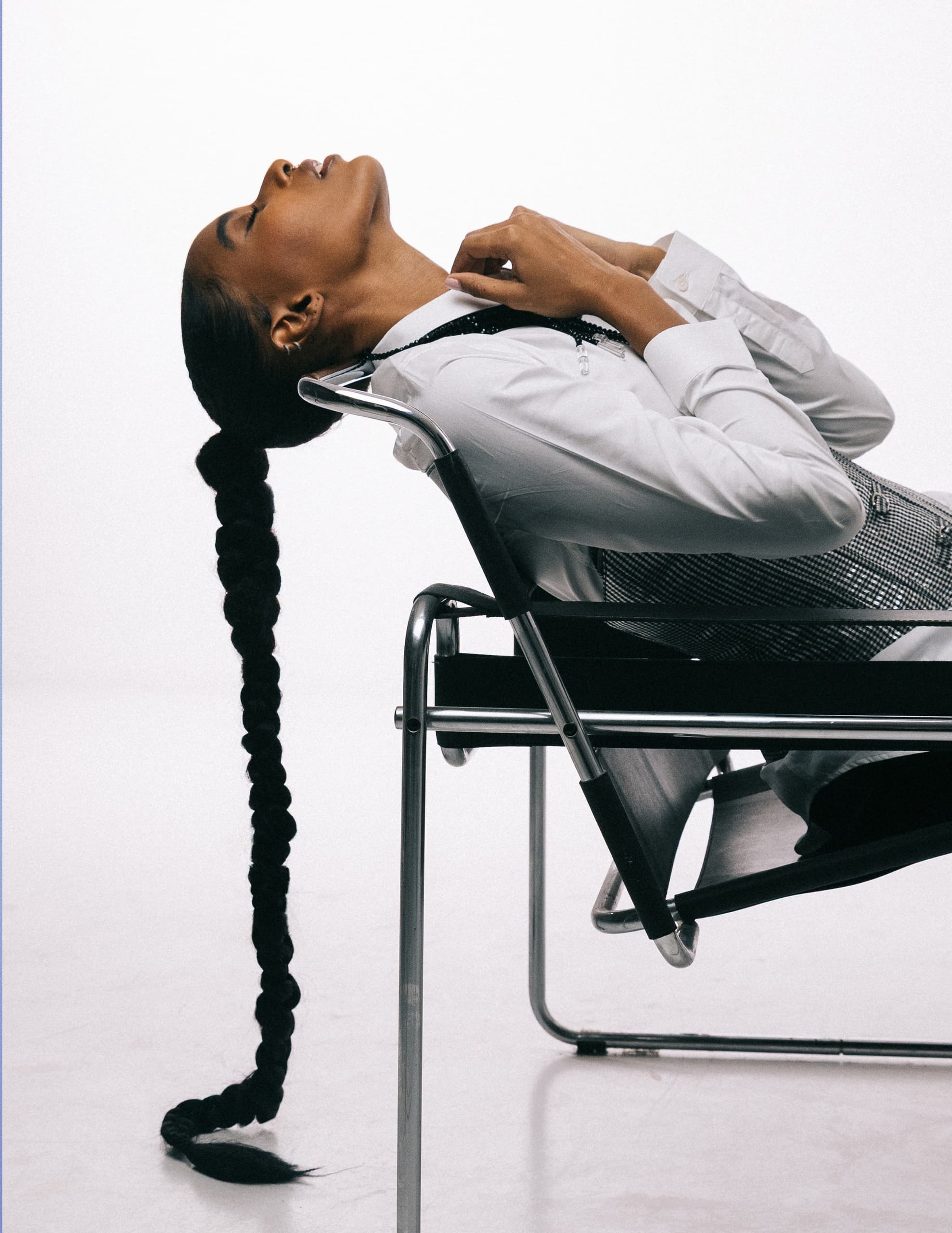 Person relaxing in chair, long braid and stylish outfit, modern minimalist setting.