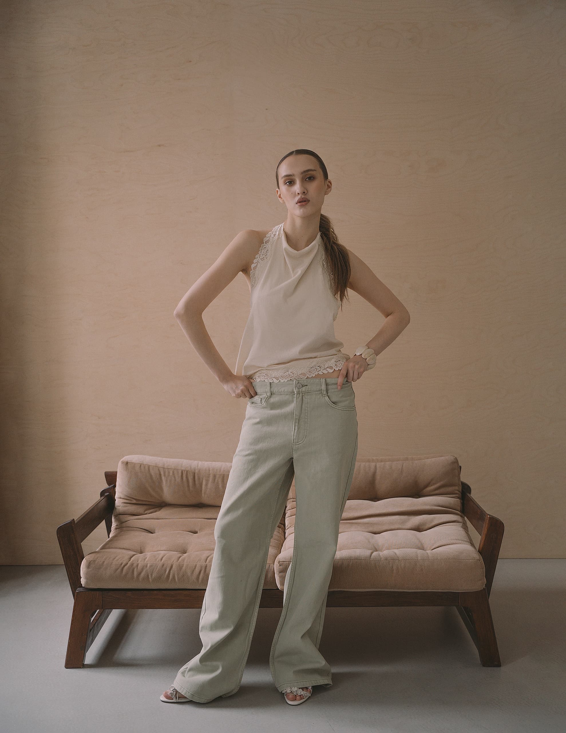 Fashionable woman posing in casual beige outfit in front of a wooden couch.