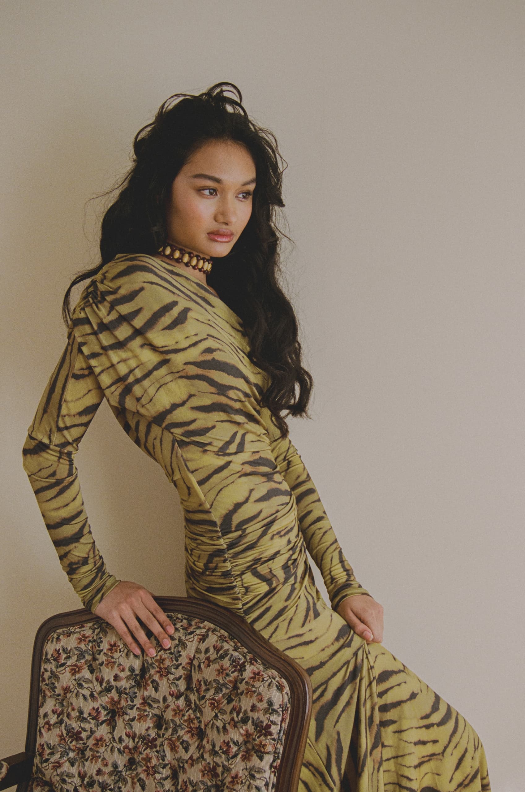 Model in stylish tiger-print dress leaning on floral chair.