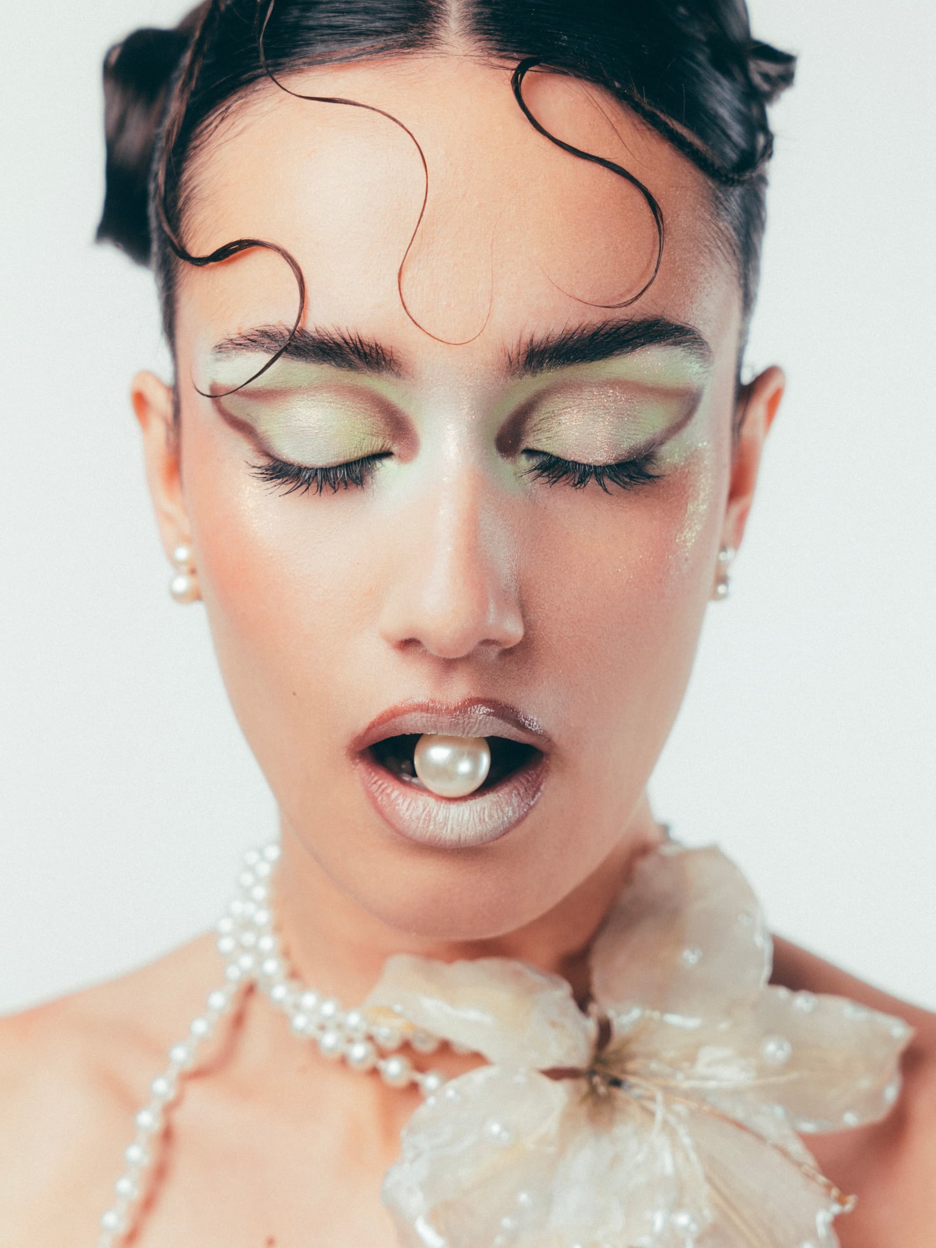 Elegant woman with pearl makeup, gloss lips, and floral accessory.
