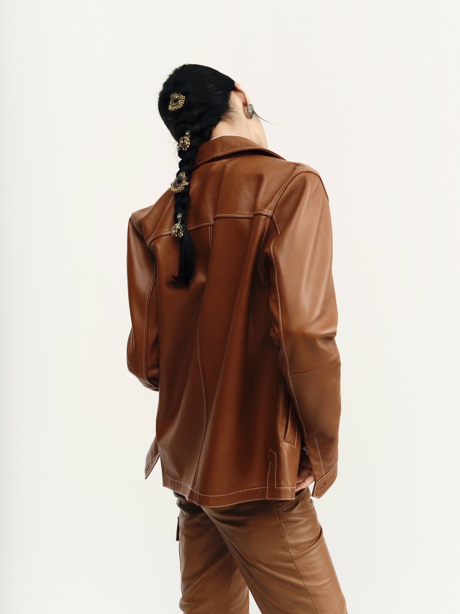 Woman in brown leather outfit with braided hair adorned with gold accessories.