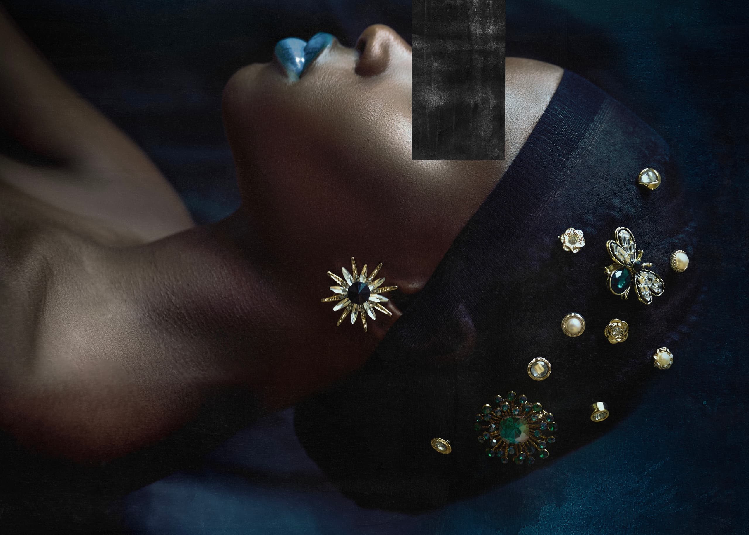 Elegant model with blue lips and ornate jeweled headpiece.