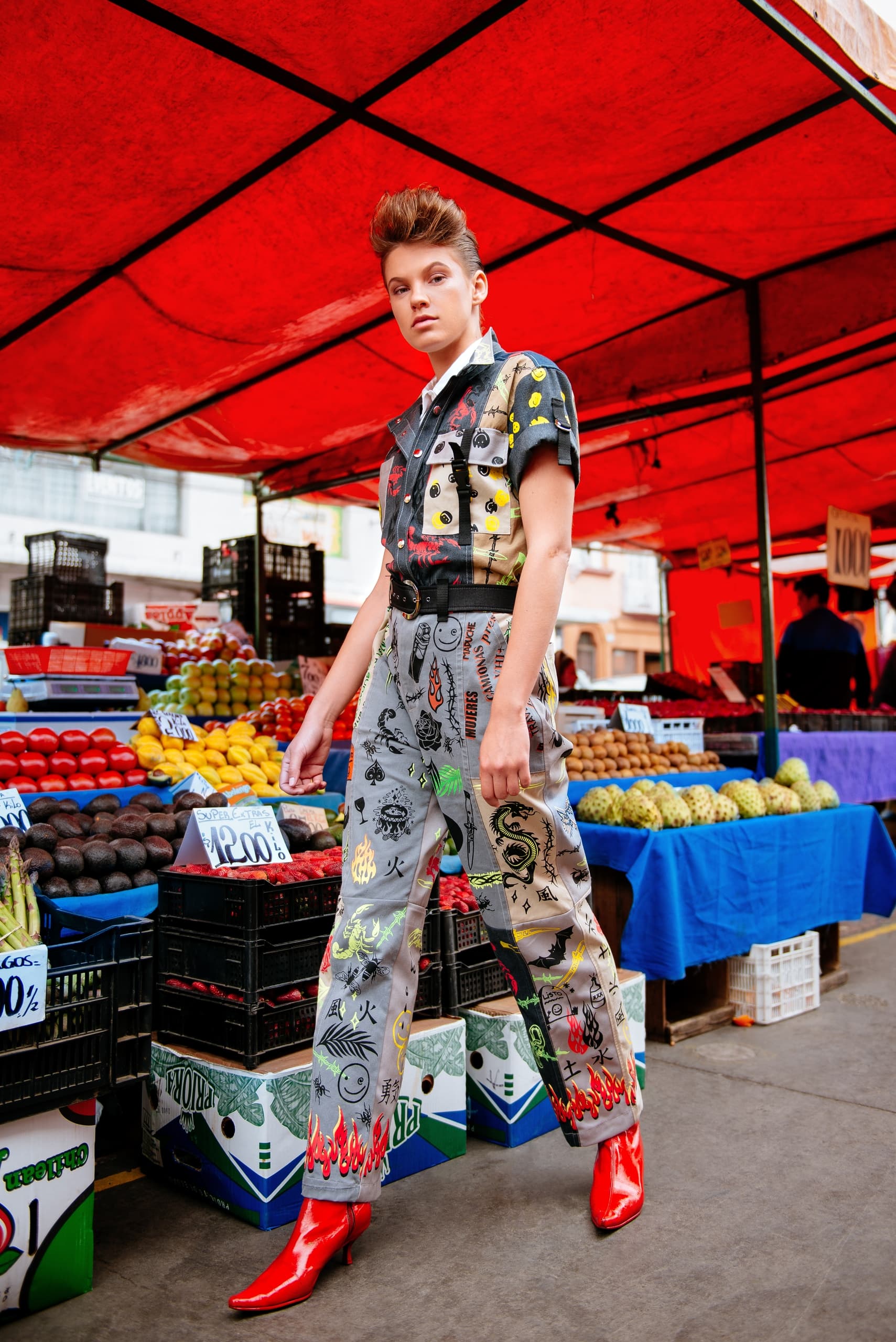 Fashionable person in colorful outfit and red boots at a vibrant fruit market.