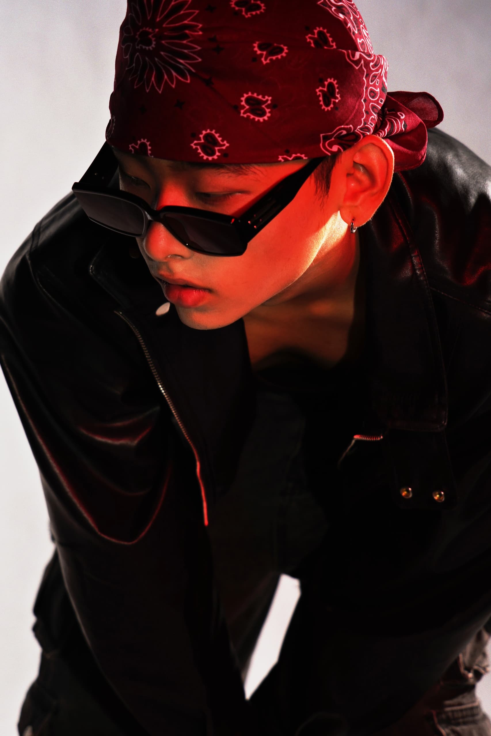 Man in leather jacket, red bandana, sunglasses in dramatic lighting.