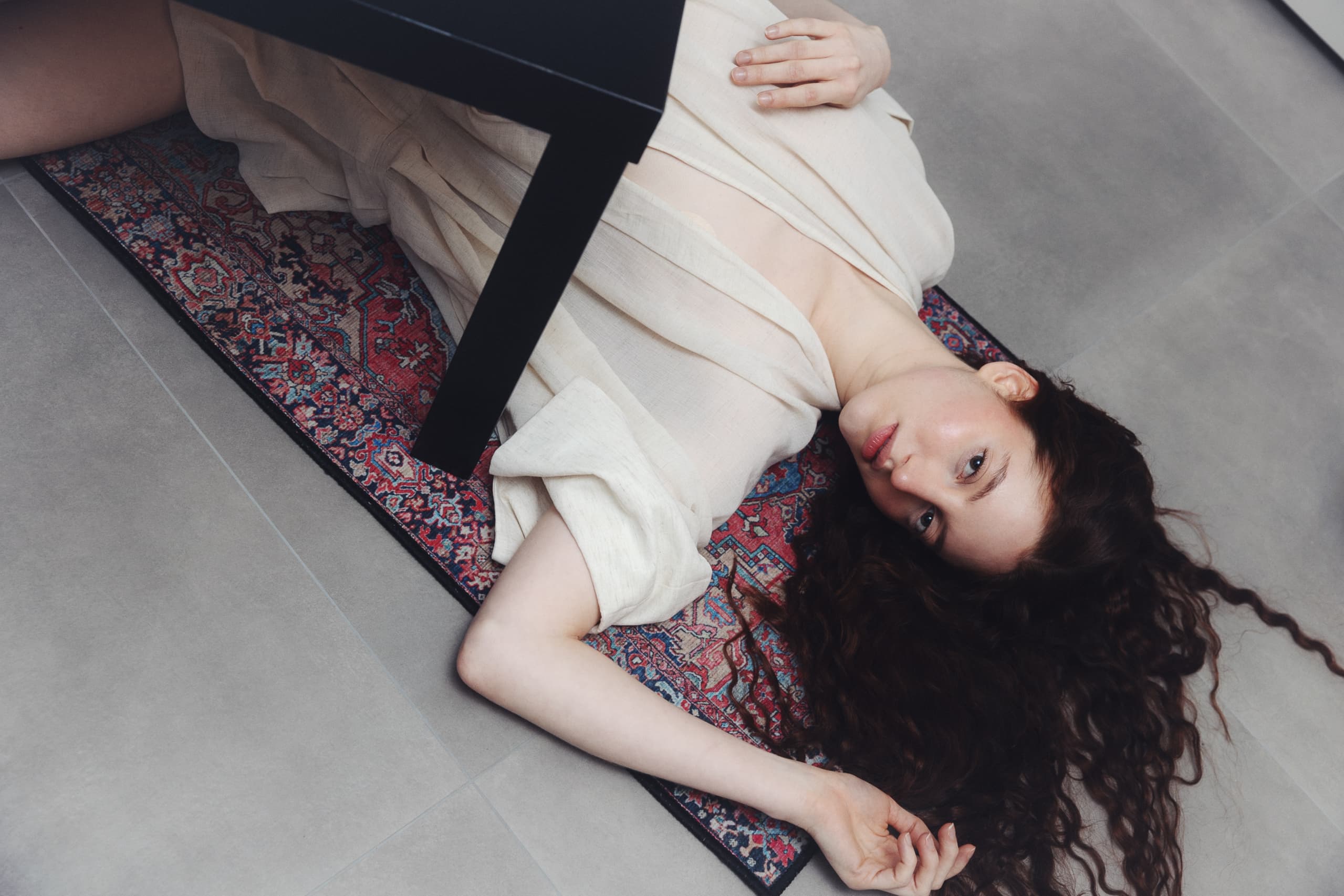 Woman lying on a patterned rug, looking up with captivating expression.