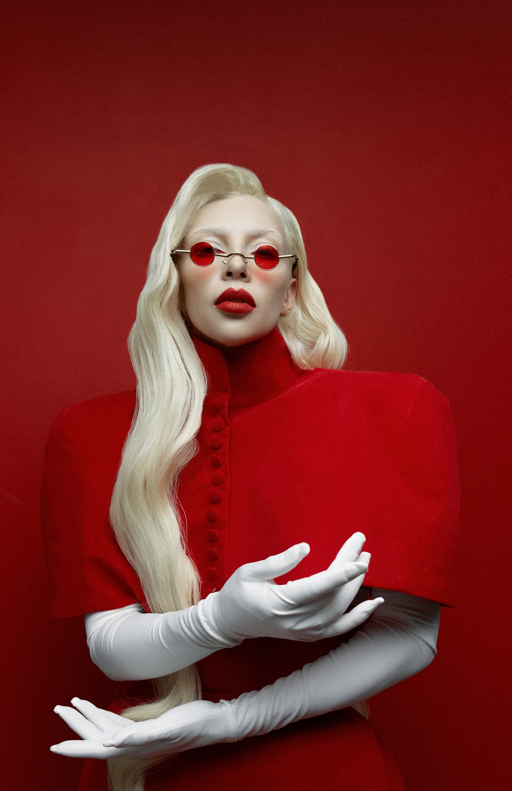 Fashionable person in red outfit and sunglasses, posing against matching red background.
